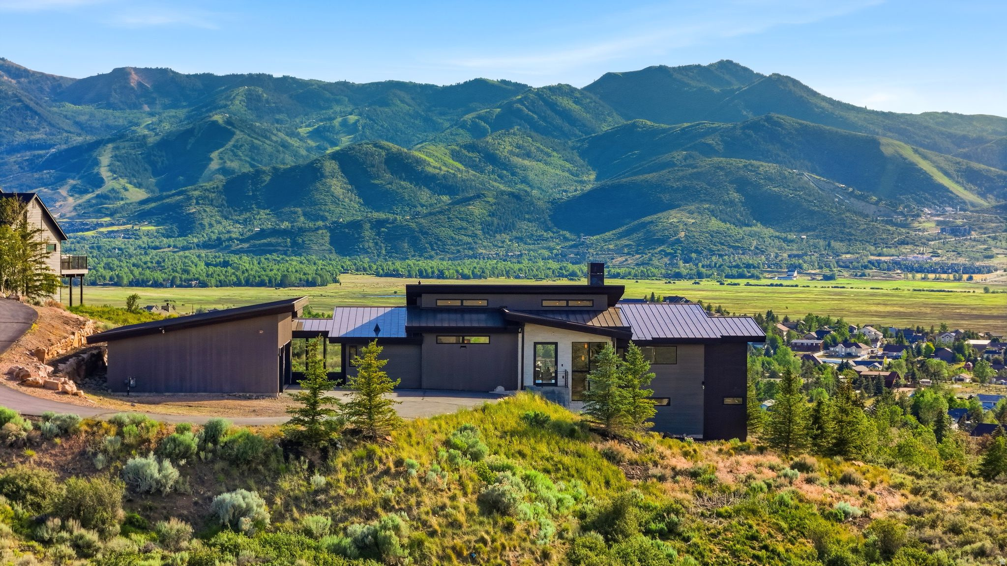 Set on 2.55 private acres, this striking contemporary residence seamlessly blends indoor and outdoor living, creating a lifestyle defined by light, space, and breathtaking mountain views. Designed to capture its extraordinary setting, walls of glass frame panoramic vistas, while oversized sliding doors open the main living spaces to an expansive terrace, dissolving the boundary between home and nature. Summer evenings unfold against spectacular sunsets over the Swaner Preserve. Gather around the fire beneath a canopy of stars, unwind in the hot tub after a day of adventure, or enjoy morning coffee as the valley comes to life. Whether entertaining a crowd or savoring quiet moments, every space is designed to elevate daily living. Sleek modern architecture is balanced by warm, inviting interiors. The open-concept great room serves as the heart of the home, where soaring ceilings, abundant natural light, and dramatic views create a setting that is both sophisticated and comfortable. The chef's kitchen, complete with an oversized walk-in pantry, is designed for effortless entertaining while keeping family and guests connected. The main-level primary suite is a private retreat featuring a spa-inspired ensuite bath, generous walk-in closet, and tranquil mountain views. A dedicated office offers an inspiring workspace surrounded by natural beauty. The walkout lower level is ideal for family and guests, featuring a second ensuite bedroom, two additional bedrooms, a full bath, and a spacious family room perfect for movie nights, gatherings, or multigenerational living. An oversized three-car garage provides ample storage for vehicles, outdoor gear, and recreational equipment, making it easy to embrace the mountain lifestyle. Private yet connected, modern yet timeless, this is more than a home--it is a place where architecture and nature exist in harmony, and every season brings a new perspective.