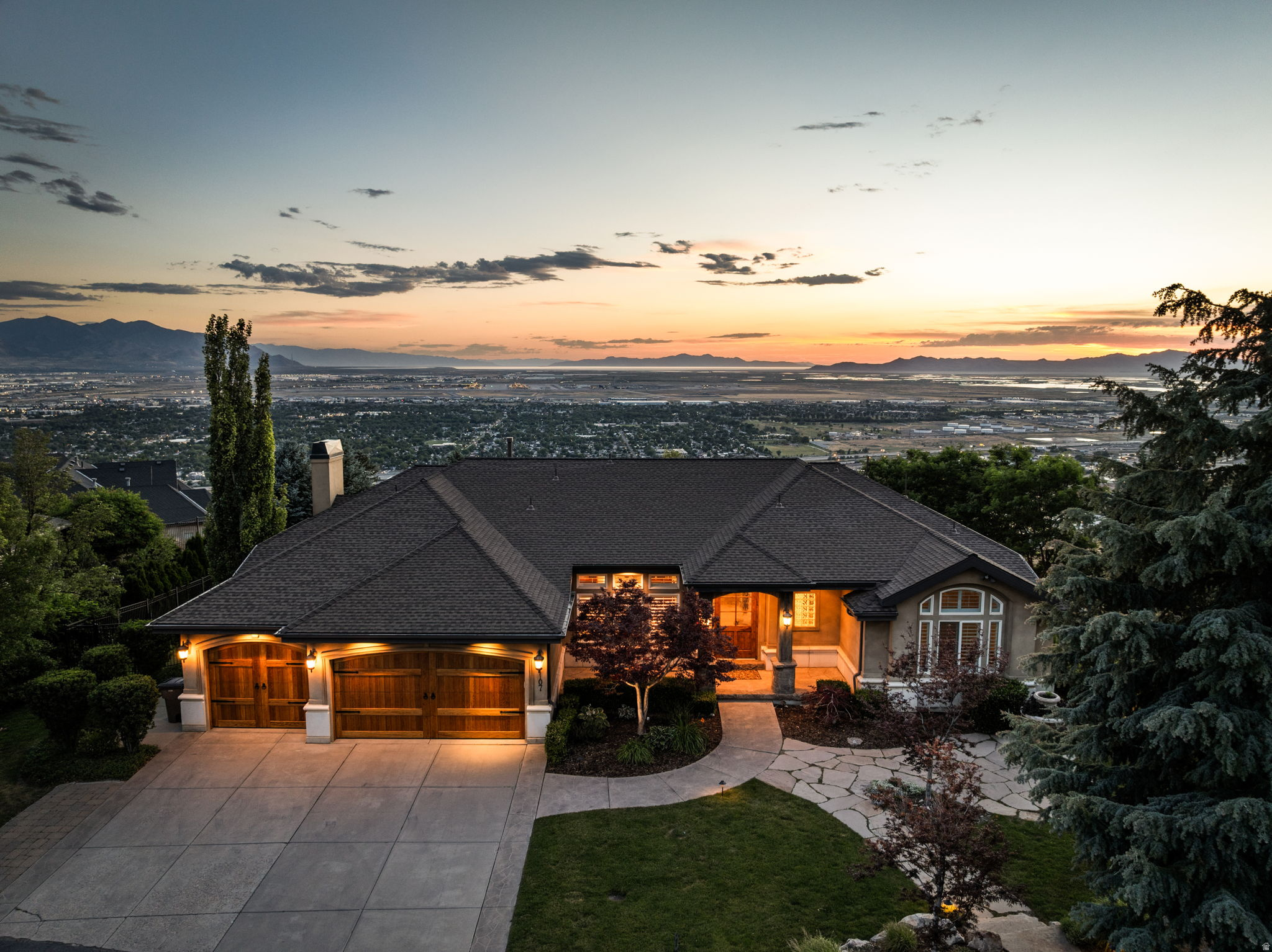 High above the Salt Lake Valley, behind the private gates of Dorchester Pointe, this remarkable walkout rambler blends timeless architecture with sweeping views stretching from Ensign Peak to the Great Salt Lake. Situated on a private .71 acres, the 6,343 square foot residence was thoughtfully designed for effortless main-level living while offering generous spaces for entertaining. Natural hardwood and travertine flooring, soaring ceilings, two fireplaces, and a wet bar create sophisticated interiors, while the chef's kitchen, appointed with Wolf and Sub-Zero appliances, dual dishwashers, and a built-in Miele coffee station, opens directly into the home's gathering spaces. The primary suite is a true retreat, featuring a private view deck, a spa-inspired bath with a steam shower and air-jetted soaking tub, and a generous walk-in closet. The fully finished walkout lower level expands the home's versatility with a second kitchen, expansive recreation spaces, and direct access to beautifully landscaped grounds. Mature pines, a cascading waterfall, lush gardens, and a secluded hot tub patio create an outdoor sanctuary that feels worlds away while remaining just minutes from the city. An exceptional opportunity to own a beautiful home in a one-of-a-kind location.