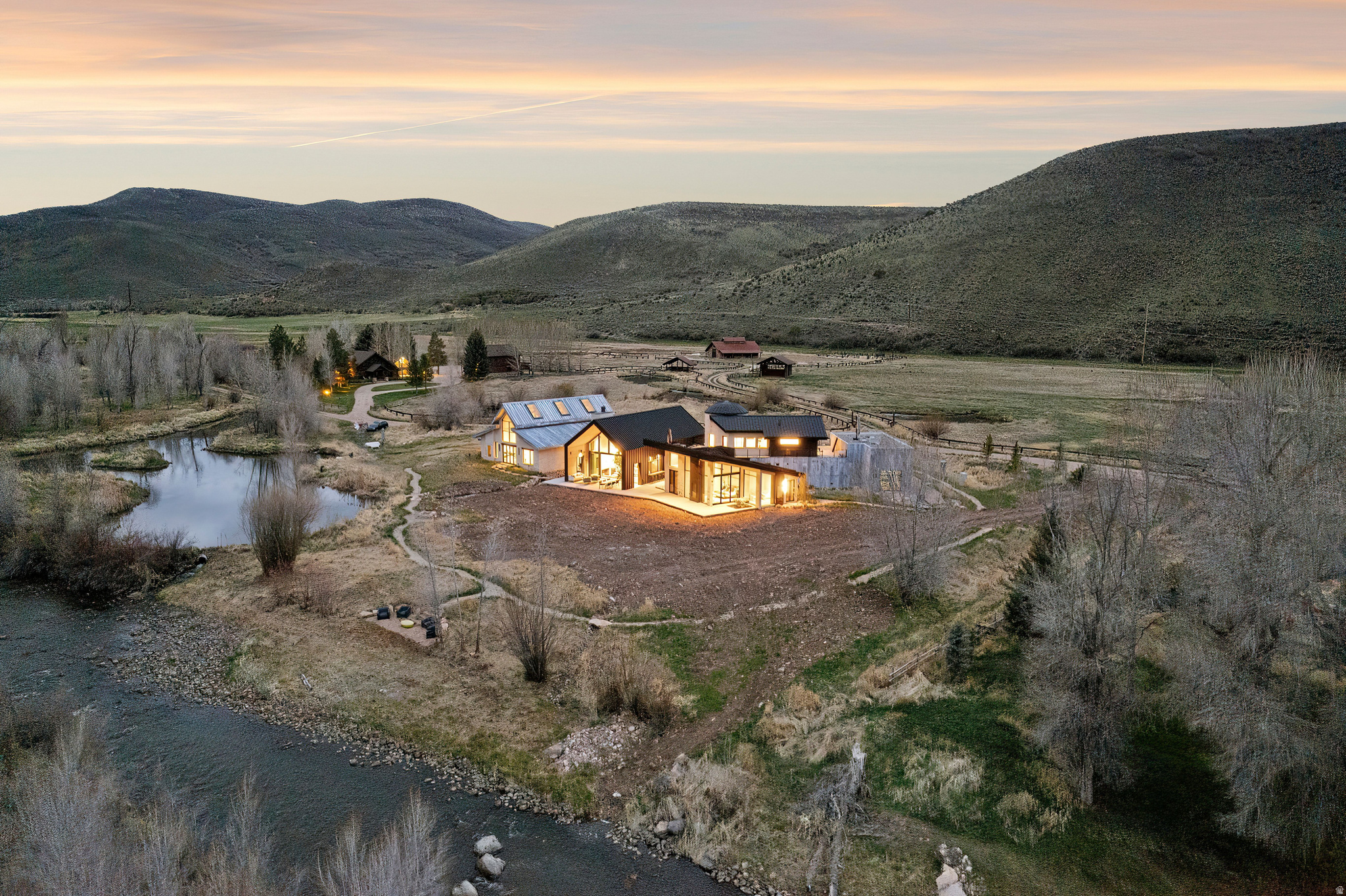 Stark Ranch is a modern equestrian wellness estate set on approximately 21 private acres in Peoa, Utah, just minutes from Park City, Deer Valley, and Deer Valley East Village. With approximately 450 feet of direct Weber River frontage, this riverfront property offers fly fishing access, irrigated pasture, open land, and year round outdoor recreation in a refined modern ranch setting. Designed by Park City architect Rick Brighton, the 6,460 square foot residence blends classic agrarian forms with contemporary architecture. Three distinct structures define the design, including a barn inspired main living wing, a stone clad silo with a dedicated yoga and wellness studio, and a secondary barn connected by a dramatic glass overpass. Steel, glass, and natural wood finishes pair with oversized sliding doors and floor to ceiling windows for seamless indoor outdoor living and river and mountain views. The home offers five bedrooms and seven to eight bathrooms, including a primary suite with fireplace, private sitting area, and spa bath. Wellness amenities include a yoga studio, sauna, hot tub, fitness space, and rock climbing wall. Heated equestrian facilities, water rights, and direct river access complete this rare modern ranch retreat designed for legacy ownership.