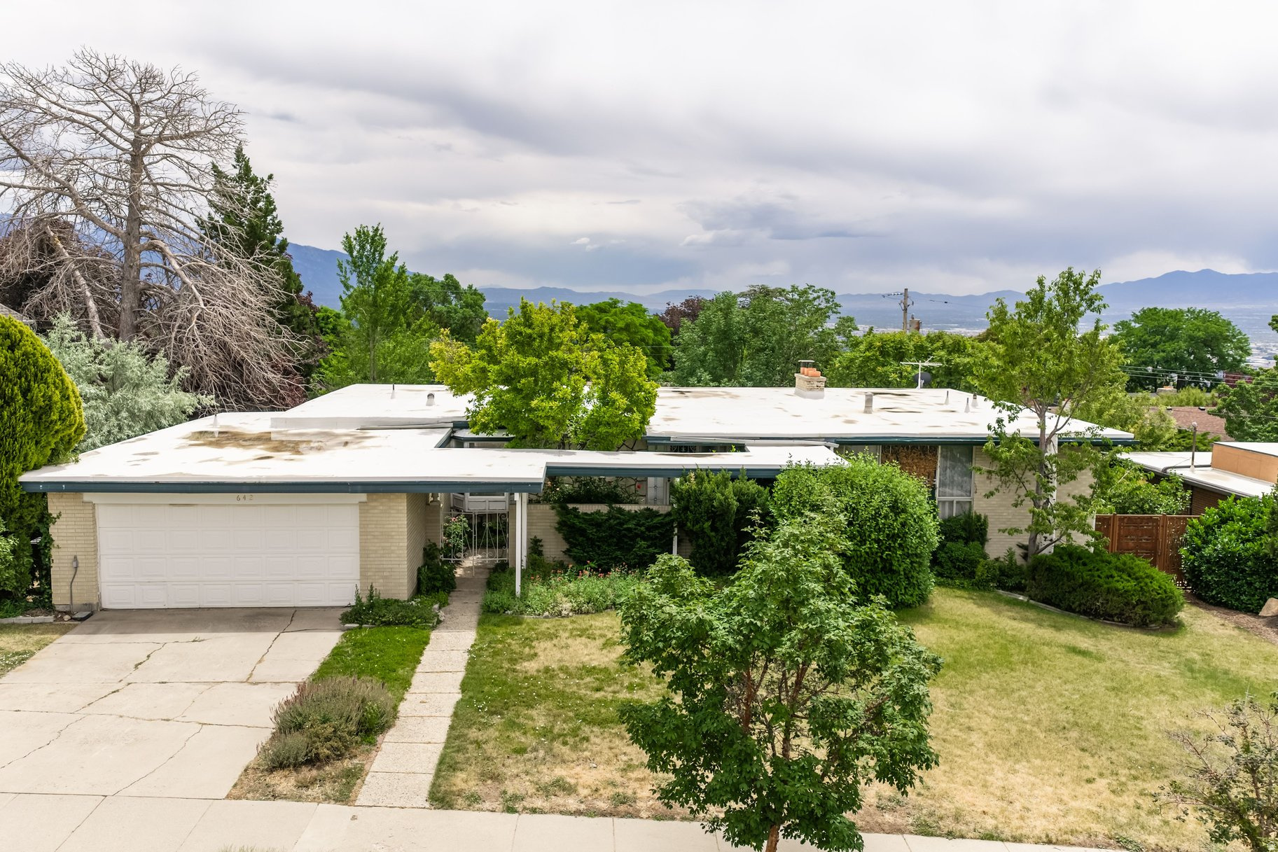 Design aficionados often say they'd rather have an original home than a poorly executed flip, and this home is exactly the kind of authentic mid-century residence that's becoming increasingly difficult tofind. Tucked within the coveted Northcrest Subdivision in the high Avenues, the home rests on a generous 0.28-acre lot, offering more than a quarter acre of mature landscaping, privacy, and a peaceful setting above the city.Before you reach the front door, this home invites you to slow your pace. A gated entry courtyard, lined with a charming stone wall and flourishing rose bushes, leads you along a tranquil garden path. Lush flowering shrubs tucked behind the gate create an intimate arrival experience -- a quiet transition from the outside world before you ever step inside. Inside, the home's original mid-century bones speak for themselves. Astriking terrazzo fireplace anchors the wood-paneled living room, while walls of glass frame the surrounding greenery and bathe the interior in natural light. Rich hardwood floors extend through much of the main level, where the thoughtful floor plan includesa primary bedroom along with two additional bedrooms.Just beyond the living spaces, a covered wood deck overlooks an exceptionally private backyard shaded by mature trees and established landscaping only time can create. As a bonus,theentrance to the Bonneville Shoreline Trail is directly across the street, providing immediate access to miles of hiking and biking with panoramic valley views. Lovingly cared for over the years, this home offers the rare opportunity to become the next steward of a mid-century property. Whether your vision is a careful restoration or a designer renovation, the possibilities begin with an exceptional foundation.