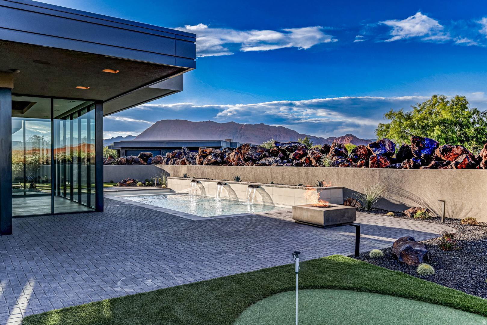 Welcome to Entrada at Snow Canyon Country Club, where luxury meets the dramatic landscape of Southern Utah. This architectural triumph, brought to life by McQuay Architects and the renowned Shakespeare Development Group, is a custom-built, single-level sanctuary. Freshly completed in late May 2026, this 4,229-square-foot contemporary estate sits on a premium 0.47-acre lot, commanding spectacular, unobstructed panoramic views of Snow Canyon State Park, Red Mountain, and the Pine Valley peaks. Positioned in the highly sought-after Chaco South neighborhood, this 4-bedroom, 4.5-bathroom custom sanctuary offers immediate proximity to the world-class amenities of the Entrada Country Club, pairing an elite lifestyle with Southern Utah's most dramatic red rock scenery. From the moment you arrive, the custom iron ''pivot'' front door makes a striking impression, opening to reveal a lava garden w/ a twin-fountain water feature. Inside, soaring recessed ceilings and strategic upper transom windows flood the home with natural light, highlighting the white oak engineered wood floors and the large-format 24x48 gray porcelain tiles. Extra-tall 7.25 in baseboards frame the solid-core doors, which are outfitted with premium Emtek hardware. For effortless living, the entire residence features full Control4 automated electrical and smart-home programming, managed from a centralized media closet, alongside a built-in central vacuum machine and premium Fanimation ceiling fans throughout. The kitchen is a masterclass in custom design, showcasing a dramatic double-waterfall island topped with honed marble. Fully wrapped in under-counter perimeter cabinets for maximized storage, the kitchen boasts ultra-sleek, consistent Venuti high-end Thermally Fused Laminate (TFL) cabinets featuring upgraded gray interiors, dovetail wood-grain drawers, and premium Blum soft-close hardware. A hand-pressed Zellige porcelain gray tile backsplash stays completely seamless thanks to hidden, under-cabinet More... plug strips. High-end culinary tasks are met with a luxury suite of Sub-Zero, Wolf, and Miele appliances, including a 48-inch 6-burner Wolf stove beneath a custom plaster range hood, a 36-inch Sub-Zero refrigerator and freezer, a Wolf double oven with an integrated steam oven, a microwave drawer, two Miele dishwashers, and a built-in KitchenAid icemaker. Ultra-durable Blanco "Silgranit" sinks are paired with upgraded Delta faucets and a Reverse Osmosis water filtration system, while a discreet, high-capacity butler's pantry keeps prep work out of sight. The split floor plan ensures absolute privacy, offering walk-in closets in 3 of the bedrooms and covered sitting patios off 3 of the 4 bedroom suites. The primary wing is a private resort unto itself, featuring a customizable fireplace, 4 built-in decorative shelves, and expansive views of the backyard oasis. The primary bathroom offers sleek marble countertops and 2 hidden medicine cabinets seamlessly integrated into the mirrors, with shower shelves left ready for the buyer's exact height specifications post-closing. Just off the bathroom, the oversized boutique dressing closet features its own massive central storage island, extensive upgraded cabinetry, and a dedicated, stackable laundry station--supplementing the home's spacious main laundry room. The resort-caliber backyard is an entertainer's dream, completely secluded from the road by stacked lava boulders and a stucco privacy wall. The outdoor oasis centers around a 14'x37' heated saltwater pool with a motorized electric cover, automatic in-floor cleaning jets, and an attached spa, all framed by a 24-inch raised beam cascading with 3 waterfalls. Lush, upgraded desert landscaping with mature trees and bushes surrounds a professional 3-hole putting green, a built-in BBQ station, and 2 exterior fireplaces. Coming inside from the garage, a dedicated mudroom features a built-in water bottle filling station. The expansive 4-car automotive garage is highly upgr