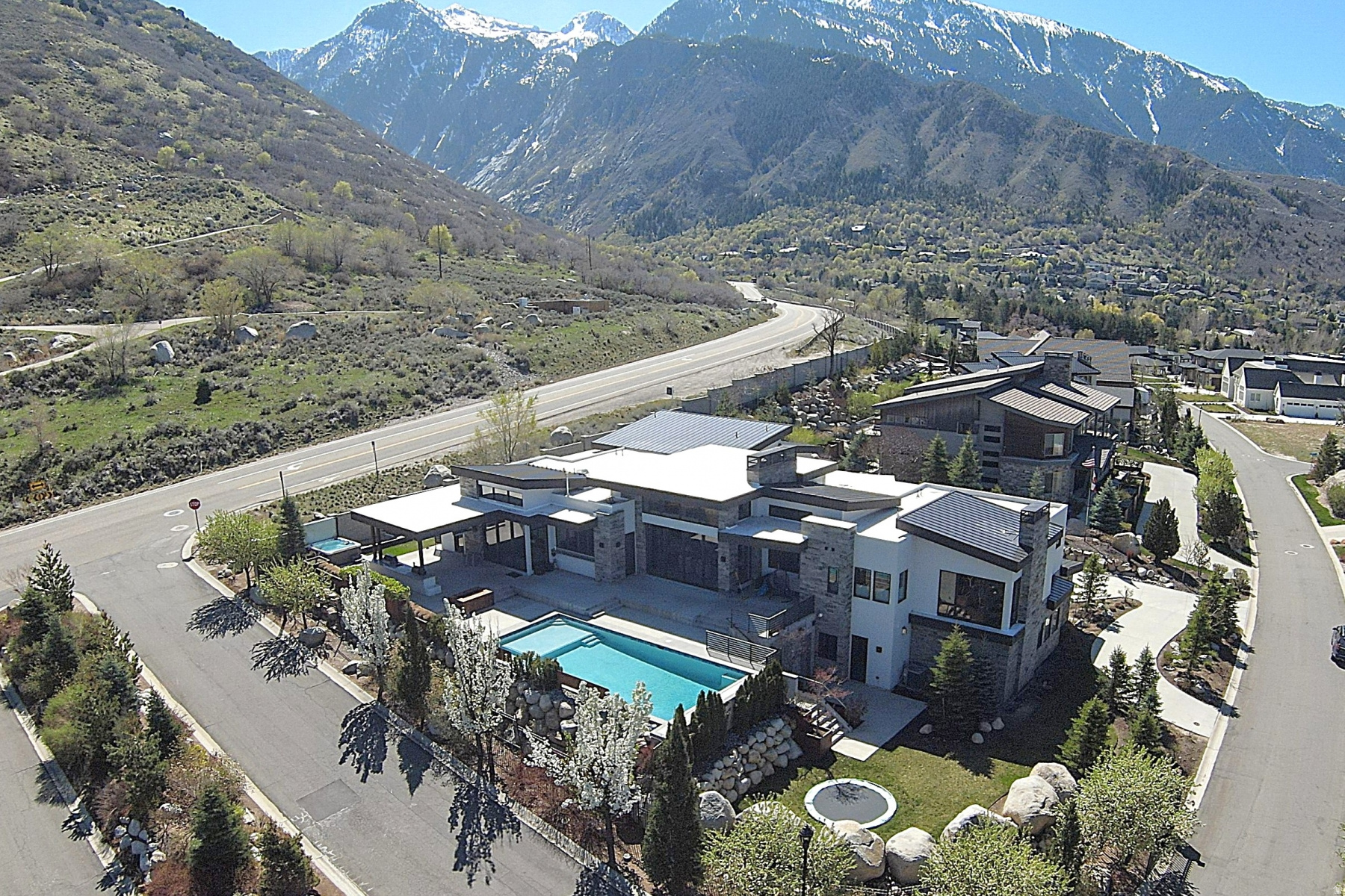 Floor-to-ceiling glass, sweeping mountain and city views, and a true resort-style backyard define 9351 S Granite Vista Dr #1, a modern mountain home in the gated Granite Oaks setting of RADIUS CURVE. Set on .72 acres near the base of Little Cottonwood Canyon, this 2018 residence blends bold architecture with the relaxed rhythm of Salt Lake County canyon living. Inside, 6 bedrooms, 8 baths, and 8,066 square feet create generous space to gather, recharge, and spread out. The great room is anchored by a DaVinci fireplace and framed by expansive sliding glass doors that draw the views directly into the home. A gourmet kitchen with high-end appliances, abundant counter space, and a butler's pantry connects seamlessly to the dining and living areas for effortless everyday function. The main-level primary suite captures the same dramatic outlook through floor-to-ceiling windows and features a gas fireplace, refined en-suite bath, and dual closets. Four additional main-level bedrooms include en-suite baths, while the lower level adds a guest bedroom, sports court, and gym. Outdoor living is equally memorable, with a pool, hot tub, outdoor kitchen, heated covered patio, in-ground trampoline, and sandbox designed for year-round enjoyment. An oversized 5-car garage with capacity for up to 9 cars adds exceptional flexibility. Located in the 84092 corridor near Sandy and Cottonwood Heights, approximately 7 miles from Snowbird Resort and convenient to canyon trails, downtown Salt Lake City, and the airport, this is an extraordinary foothills retreat ready to experience in person.