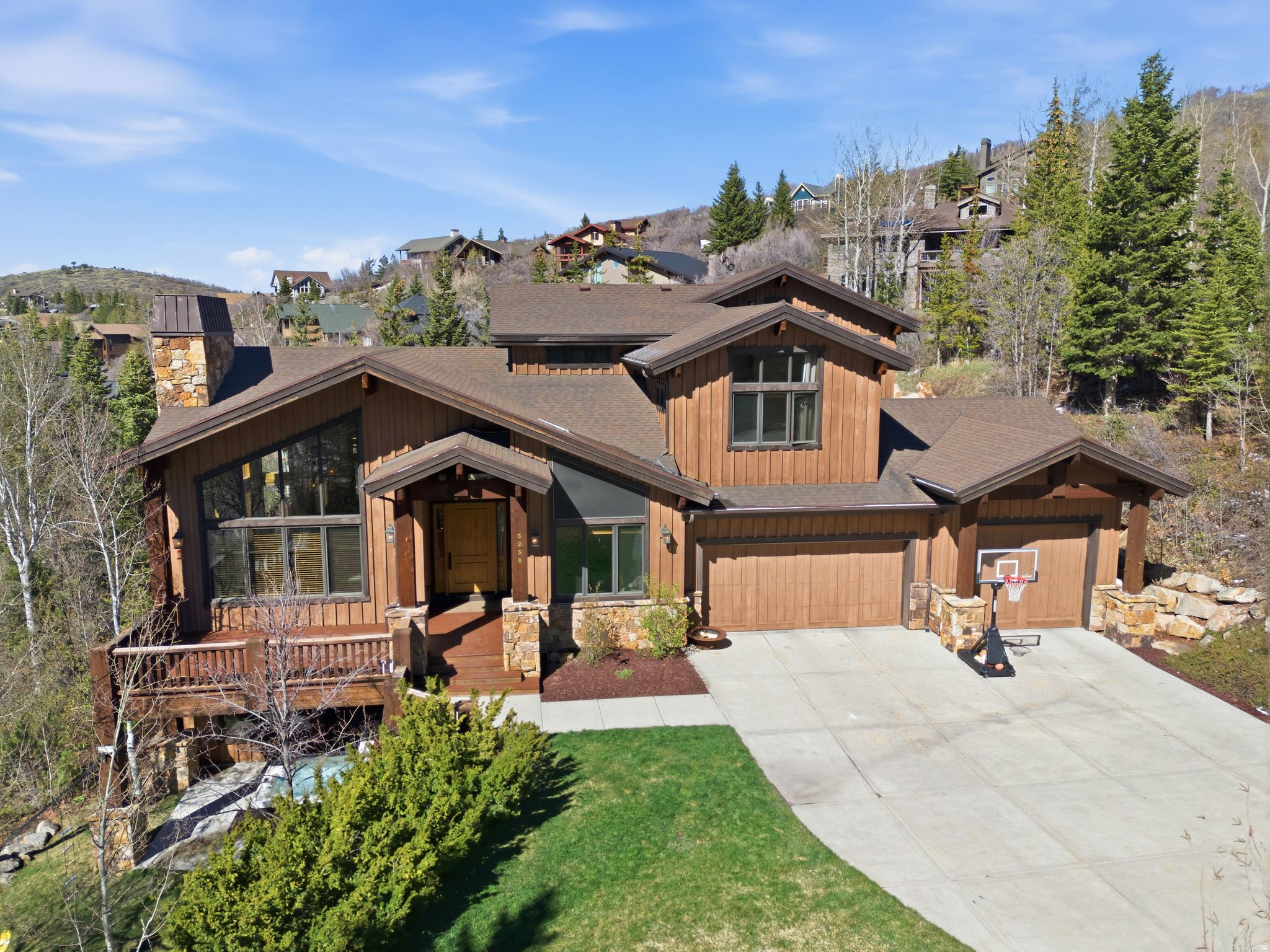 Beautifully built in 2006, this custom home sits on a private upper Pinebrook lot with a flat driveway and a rare 4-car attached garage. The main level features a stunning great room with soaring vaulted ceilings, wood floors, abundant windows, and a dramatic two-story wood-burning fireplace. An informal dining area flows naturally from the great room into the high-end kitchen which includes Sub-Zero and Wolf appliances, a full-size wine fridge, walk-in pantry, breakfast bar, and a charming dining nook. The main level also offers a bedroom with an ensuite three-quarter bath, a dedicated home office off the entry, and a spacious mudroom and laundry room. Upstairs, the primary suite includes a gas fireplace, private deck, large closet, and a luxurious marble five-fixture bathroom. A second bedroom with its own ensuite bath completes the upper level. The walkout lower level provides a generous family room with a walk-behind full bar, two additional bedrooms and a full bath, a large theater room, and finished interior storage. Outdoor living is exceptional with inviting deck space, attractive front-yard landscaping, and a private flat patio and play area.