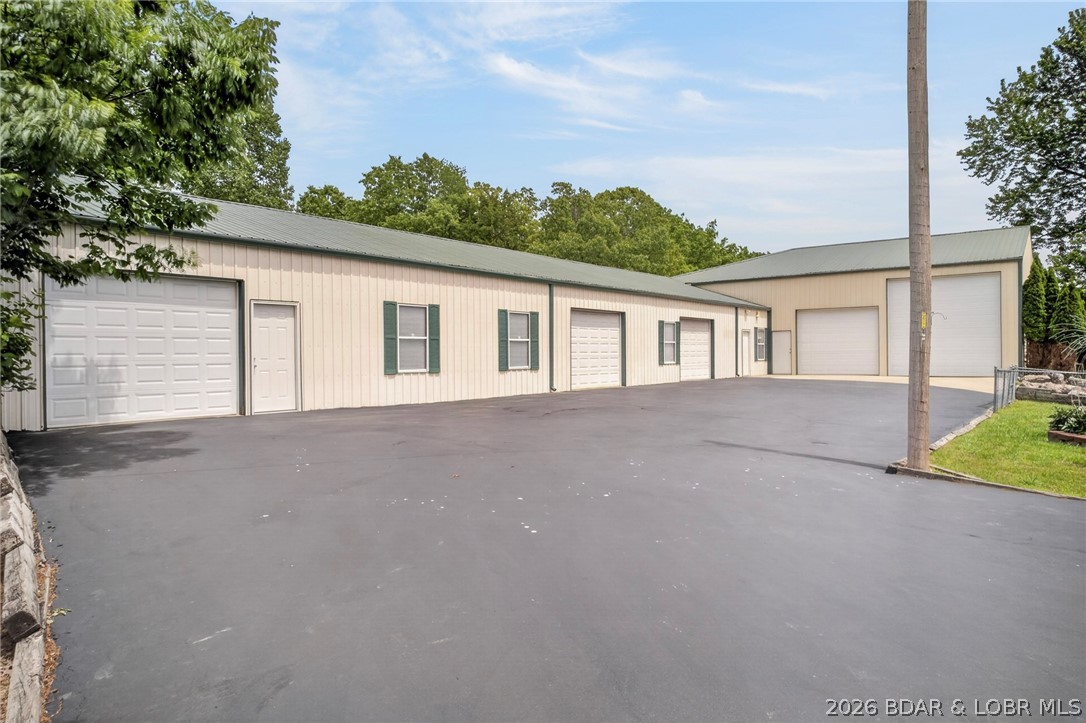 LIVE, WORK & INVEST! Exceptional mixed-use opportunity offering over 7,800 sq ft of shop space paired with a versatile residential home that can be owner-occupied or rented for additional income. The impressive shop features a 100x50 three-bay area plus a 70x40 RV storage bay, easily accommodating 15+ vehicles, along with a dedicated workshop and bathroom—ideal for business operations, storage, or hobby use.
Situated on 4+ acres just 10 minutes from Osage Beach, this property combines privacy with convenience, making it well-suited for contractors, automotive businesses, or investors seeking flexible use.
The home offers an open floor plan with main-level living, a bright four seasons room, and access to a fenced backyard with pool, deck, and outdoor entertaining space. The lower level provides additional living area with a bedroom, full bath, walkout access, wood-burning stove, and ample storage. This one is a rare find!!