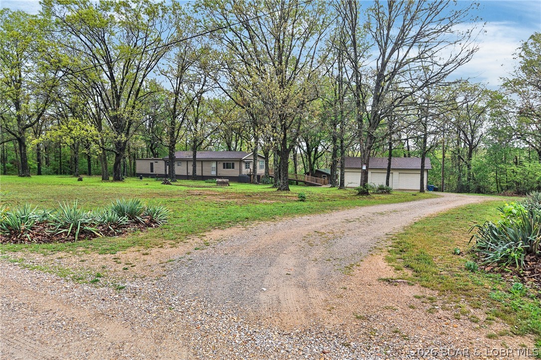 This home consists of a mobile with an addition on a concrete foundation, nestled away from the road in a BEAUTIFUL PARK-LIKE SETTING ON 6.01!! Including the addition to the original homesite, it now offers over 1,600 sq ft of living space! The layout - 3-bedroom, 2-bath, a spacious living room, and a beautiful updated kitchen that includes stainless steel appliances, and a dining room, PLUS a lovely sunroom W/ a built-in bench, A DETACHED 3-CAR GARAGE, and a lovely building great for your guests! with utilities including septic ( needs a few finishing touches), ALSO a man cave /She-shed with propane heat, water, and electric. YOU WILL LOVE THE UPGRADES, including a newer roof with a transferable warranty, a wrap-around deck with a ramp, updated LED lighting, sinks and faucets, kitchen countertops, 2Extra connections for the laundry are available (currently the 3rd bedroom is being used as a laundry area), and it could be moved.  newer LVP flooring throughout the home,&  hydrant(S) throughout the property, & located close to Bennett Spring Conservation Area, which is home to wildlife. Then enjoy hiking, hunting, camping, and trout fishing down the road at Bennett Spring Park.