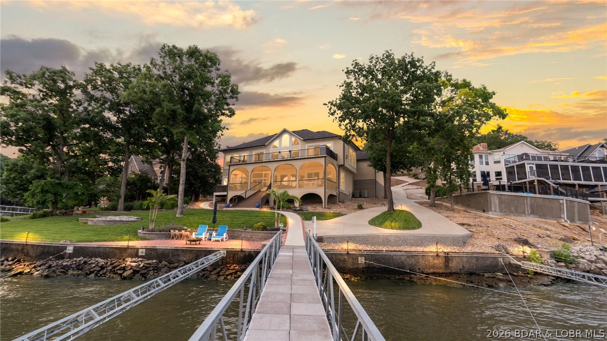 Experience exceptional lakefront living at this beautiful property in the prestigious Four Seasons community. Situated on 137 feet of prime Lake of the Ozarks shoreline, this stunning 4-bedroom, 3.5 bath residence offers approximately 4,300 square feet of thoughtfully designed living space with breathtaking main channel views. Recently updated with a new roof, refreshed stucco, epoxy garage floors, new deck railings, and professional landscaping, the home seamlessly blends luxury and comfort. The open-concept floor plan features vaulted ceilings, a spacious living area with fireplace, a gourmet kitchen, walk-in showers, jetted tub, wet bar, and a finished walkout lower level ideal for entertaining. Outdoor living is equally impressive with expansive decks, a screened porch, patio just steps from the water, and direct access to a private dock featuring two boat slips and a 4 PWC slips with lifts. Custom boat dock built for main channel living with a heavy duty C-Channels, concrete trays, and anchored to the ground! Located within the sought-after Four Seasons community, owners enjoy access to pools, playgrounds, walking trails, gym & premium amenities.