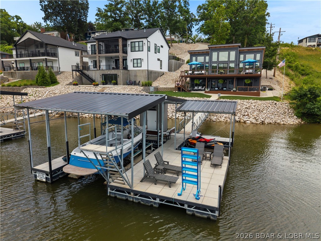 Contemporary luxury meets effortless lake living in this stunning newer construction home, perfectly positioned in the heart of Osage Beach. Showcasing striking architecture and walls of glass that frame breathtaking lake views, this thoughtfully designed, fully furnished retreat is filled with custom, high-end finishes at every turn. The open-concept floor plan is anchored by a dramatic floor-to-ceiling fireplace and a showstopping kitchen featuring waterfall quartz countertops, an oversized island, and seamless flow for entertaining. The luxurious primary suite offers a true spa-like escape with dual vanities, a beautifully tiled walk-in shower, and a spacious walk-in closet. The walkout lower level adds a second family room, creating plenty of space for hosting family and friends. Outside, two expansive decks invite you to relax and soak in the views, while the covered and uncovered dock makes enjoying the lake effortless. Just minutes from premier waterfront dining, shopping, golf, and entertainment by both land and water, this exceptional home delivers the perfect blend of modern design, luxury, and the Lake of the Ozarks lifestyle.