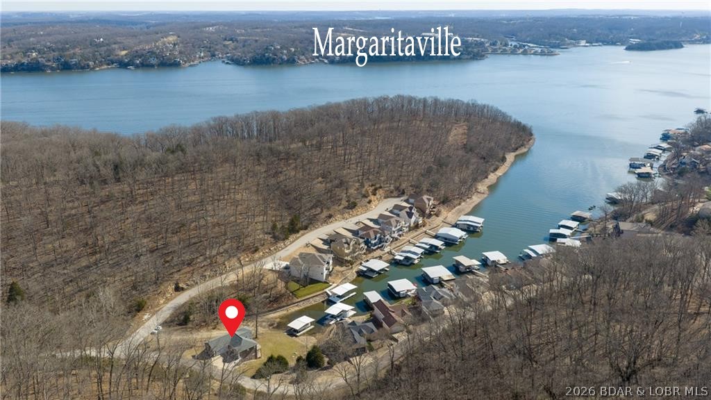 Take a look at this one! Luxury lakefront living in quiet cove - 26mm! Relax across multiple outdoor spaces, w/ gorgeous main channel views—perfect for morning coffee, sunset cocktails, & watching Margaritaville's July 4th fireworks. Just mins from the lake’s best waterfront restaurants & attractions, hop on the boat & let the vacation begin. Stunning open-concept retreat welcomes you with a grand hearth room featuring cathedral ceilings, gas fireplace, & dramatic windows framing breathtaking water views. Kitchen offers stainless steel appliances, breakfast bar, + sunny breakfast nook opens to the screened-in porch overlooking the lake. The main-floor primary suite - a private sanctuary w/ its own deck for even more outdoor enjoyment & boasts coffered ceilings, large walk-in closet, spa-inspired bath w/ double sinks + jetted tub & walk-in shower. Walk-out lower level features a spacious lakeside rec room, 3 more bedrooms including a primary-style suite w/ full bath & supersized walk-in closet. Fresh Paint. New Carpet. 12x30 dock, lift + Monark Seville 24' pontoon w/150 Yamaha outboard. Boat ramp. Paved streets-NO GRAVEL. HOA covers water/sewer. Level parking 4+ & attached garage.
