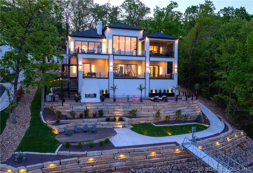 THIS is what luxury new construction at Lake of the Ozarks should look like. Perfectly positioned in a cove with main channel views at the Osage 15MM in the prestigious Porto Cima community, this custom lakeside estate delivers true resort-style living. The outdoor space is stunning—featuring a heated gunite pool w/ tanning shelf, stamped concrete decking, see-through gas fireplace & covered cabana with grill station; all surrounded by extensive, professionally designed landscaping with illuminated stonework along the 105' of shoreline, creating a striking floating effect. Inside, the living room showcases 16' high ceilings w/ an expansive quad-panel stacking glass door system, seamlessly blending indoor & outdoor living. The kitchen impresses w/ layered accent lighting throughout, custom cabinetry, quartz countertops, warming drawer, pot filler & even double dishwashers! The lower level includes a 6-sided concrete safe room ideal for a shelter, wine cellar or gun room. Additional highlights FULLY furnished, epoxy garage floor & pool bath floor, gentle driveway + additional parking. Premier location by land & water near golf, dining, entertainment, shopping & quick highway access.
