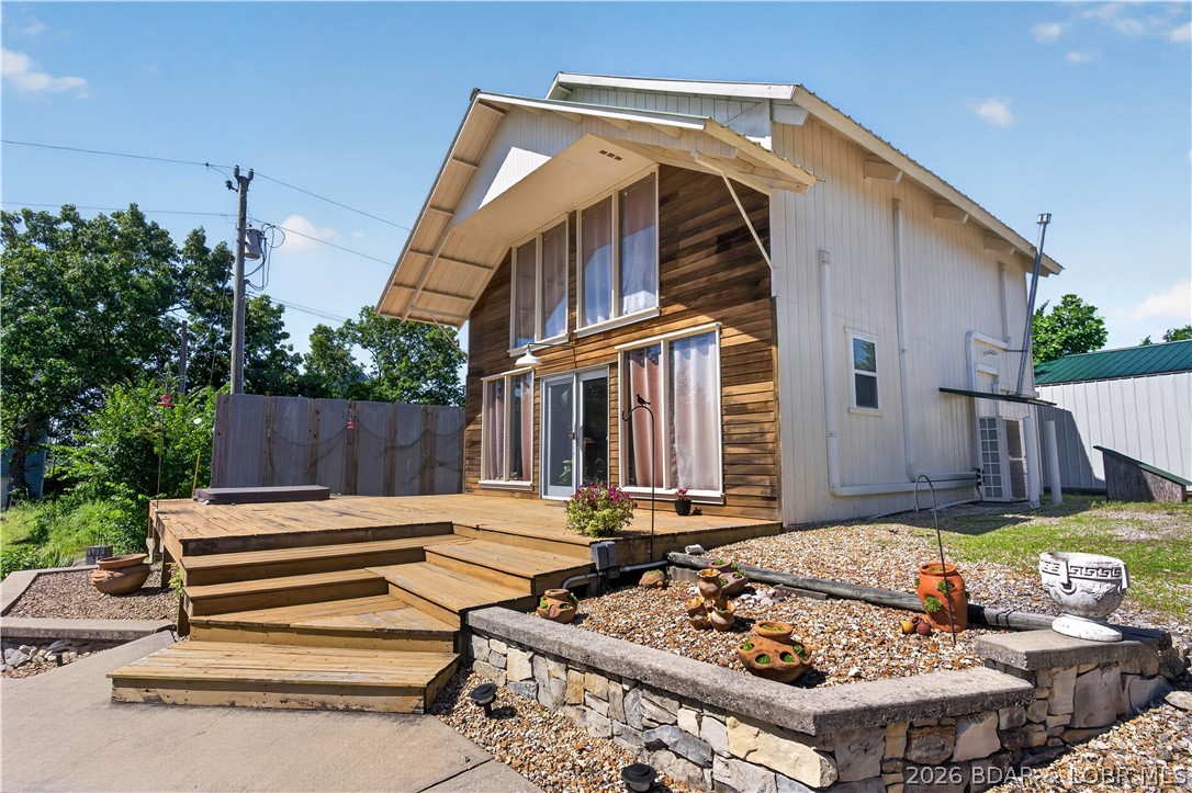 Lake of the Ozarks home with waterfront lot and 4 additional lots featuring some of the best outdoor entertaining space you'll find! This property offers ample parking along with a detached garage, carport, and additional outbuilding with a lean-to. Inside, you'll find a spacious primary bedroom, an inviting living room filled with natural light, and a welcoming kitchen perfect for everyday living or weekend getaways. Step outside to enjoy the incredible outdoor living area featuring a large deck with a hot tub, a concrete walkway leading to a built-in grill station, fire pit, and gazebo. Beautiful stonework and generous outdoor counter space create the perfect setting for hosting cookouts and enjoying evenings at the lake. A short golf cart ride takes you to the included waterfront lot, complete with a one-slip dock and swim platform and its own 1,000-gallon septic tank with 300 feet of lateral lines, making it easy to spend your days on the water and provides you the possibility of adding an additional building! Conveniently located on paved roads just a short drive from Warsaw, this property offers the perfect combination of comfort, recreation, and Lake of the Ozarks living.