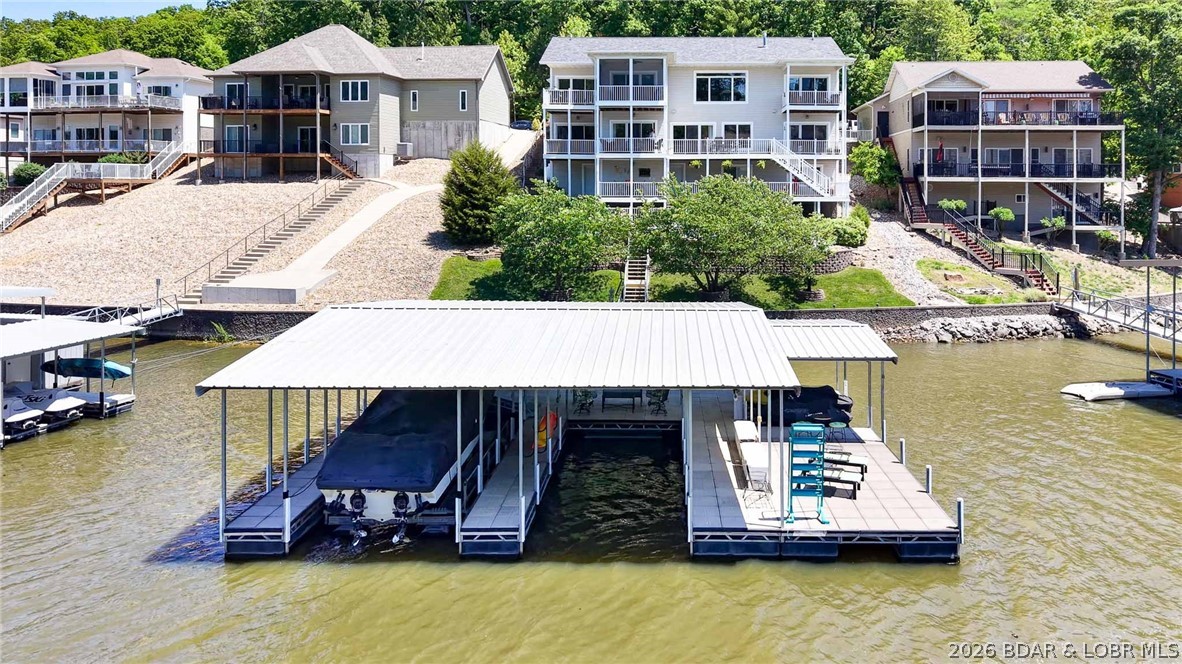 One-owner custom-built home with exceptional upgrades and spectacular lake views with cove protection and deep water! This beautifully maintained, full landscaped property includes a 3-well dock and PWC. The open main-level living area features a great room with gas fireplace with built-ins, formal dining, and spacious eat-in kitchen with upgraded appliances, Custom Shrock cabinets, screened deck and grilling area—perfect for entertaining. The luxurious Primary Suite offers a spa-like bath and walk-in closet with a private deck, plus a den/bedroom (2nd bedrm) on the main level. Lower level includes a large family room with gas fireplace, wet bar & game room, second suite, additional bedroom & bath, library area, & office (5th bedroom) Additional finished storage. The lower level offers a summer kitchen, half bath, &  finished/unfinished storage. Room for all your guests with a level driveway, central sewer, & city water. Conveniently located just minutes from town, shopping, dining, school & hospital and lake amenities. Some furnishings included. See Attachment for upgrades/improvements: New Roof, Newer HVAC & More. Furnishings list attached.