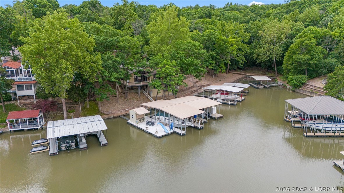 This fully furnished 4 bedroom, 4 bath lakefront home is all about living on the water—perfect as a private retreat or an income-producing vacation rental with nightly rentals allowed. The front door puts you right at the lake, with open and covered decks that invite you to linger over morning coffee and sunset dinners overlooking the water. Inside the main level’s vaulted ceilings and cozy fireplace frame the lake views, while a formal dining room, breakfast bar, and wet bar make it easy to host weekends at the lake. The main level also features an en-suite bedroom with walk-in showers and walk-in closets, giving everyone a comfortable, private place to unwind after a long day on the water, and the lower living room creates an extra hangout spot for family & friends. Just a few steps from the house, a massive dock becomes the heart of your lake life, complete with a bar for dockside gatherings, a water slide, a swim platform for lounging and jumping in, and three boat slips, the largest being a  16' x 50' slip ready for your cruiser or big-water boat. Turn-key and ready to enjoy from day one, this property delivers the easy, laid-back lake lifestyle so many people dream about.