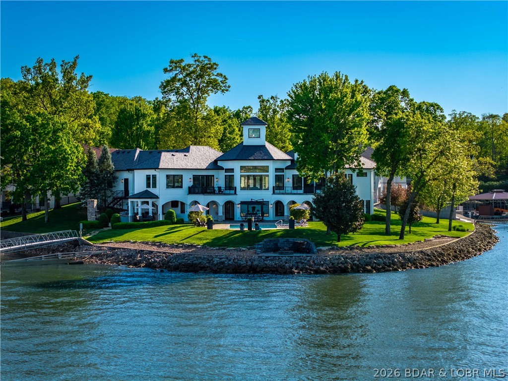 Positioned on a premier point in the prestigious Porto Cima community, this exceptional lakefront estate offers luxury, privacy, and panoramic main channel views. Boasting 464 ft. of shoreline, the property delivers an unmatched waterfront setting. Completely remodeled, the home offers over 6,000 sq. ft. of thoughtfully designed living space with five bedrooms, each featuring a private ensuite. The primary suite and a second suite are conveniently located on the main level. Designed for both elegance and easy lake living, the home offers multiple entertaining areas and sits on a level lot featuring a self-cleaning lakeside pool, outdoor kitchen, fireplace, and lakeside fire pit. The impressive rough-water dock includes 18x50 and 12x32 slips, auto doors for the bar and storage, plus a rough-water wave break. With impeccable craftsmanship and high-end finishes throughout, every detail has been carefully curated to create a sophisticated yet comfortable retreat that shows like a model home. Furnishings are included, allowing for a seamless turnkey opportunity. Enjoy all Porto Cima and Four Seasons amenities, just minutes from The Club at Porto Cima.