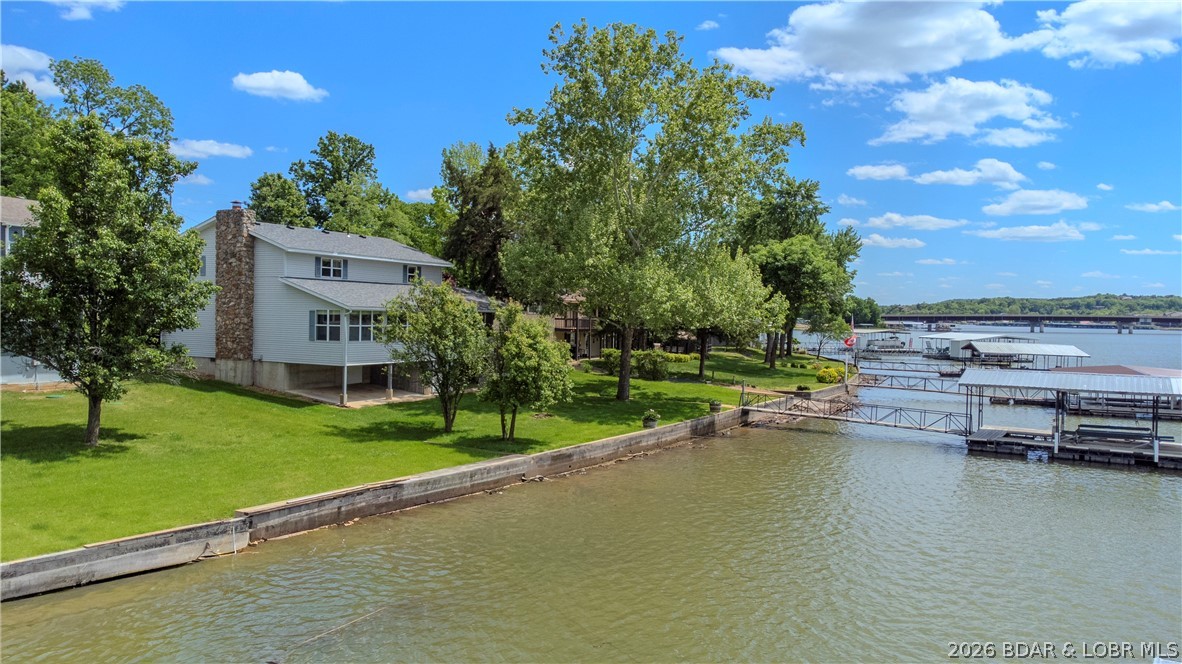When you are looking for a lawn on the lake (and it is hard to find) this home is for you!  The location does not get any better than this one!  Situated in an established LF community,  this neighborhood boasts of level driveways  into your garages, easy access to the highway, the quiet waters of the Big Niangua and being only a stone's throw to Kinderhook and Lake Valley Golf Courses. Haha Tonka is also a short drive from this home; close enough to make the stairs a part of your work out regimen in the most beautiful state park in Missouri. This spacious family home featuring 4 bedrooms and plenty of bathrooms is the ideal retreat for hosting guests or raising a family. An open kitchen and dining room space leave plenty of room for a formal dining room or  hearth room right off of your kitchen. An enclosed sun room that spans the lakeside of the home create a space that is open and bright.  The level backyard is the hallmark of this property where there is abundant room for a large fire pit, outdoor kitchen, and the perfect place to host a bean bag tournament right in your back yard that is level and invites outdoor entertaining spaces right at the waters edge.