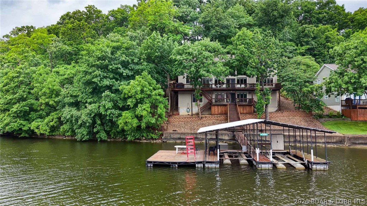 Luxury lake living meets exceptional value in sought-after Bogue Bay at the 4MM of the Gravois Arm. This furnished 5-bedroom, 5-bath lakefront retreat offers over three levels of thoughtfully designed living space, making it ideal for a full-time residence, weekend escape, or income-producing vacation rental. The main level showcases soaring vaulted ceilings, a dramatic wall of windows, an open-concept great room, formal dining, breakfast nook, laundry, and an oversized primary suite featuring a walk-in shower and an oversized soaking tub. The loft-style upper level overlooks the great room below and offers a second family room, 3 guest bedrooms, a full bath with dual vanities, and a half bath. The walkout lower level includes another family room, guest bedroom, full bath, and utility room. Just steps away, the two-well dock invites endless days on the water. Comfortably sleeping 14+ guests, this turnkey home combines breathtaking lake views, generous gathering spaces, and one of the Lake's most desirable locations.