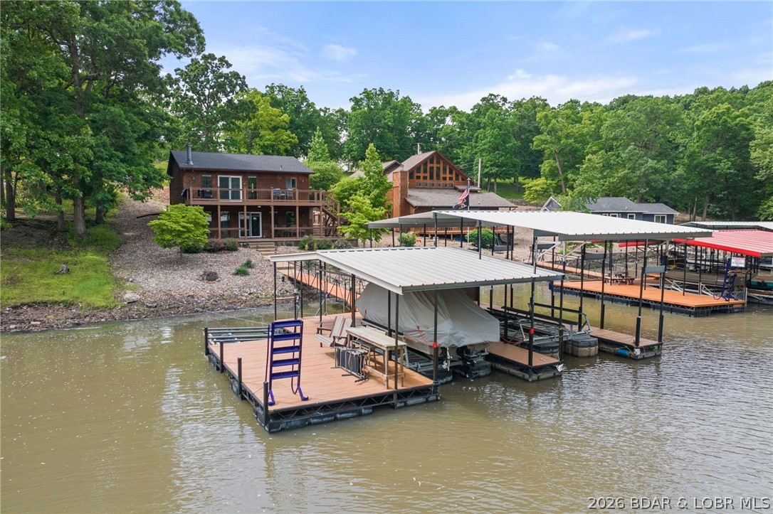 Lakefront living awaits at 2539 Robin Hood Lane, located in a quiet subdivision in Roach, Missouri. Situated at the 43 mile marker of the Osage Arm, this home features 1,792 square feet of living space across a highly functional layout. The interior offers three bedrooms and two full bathrooms, with updates that include new carpeting and fresh paint in the bedrooms. The main living level boasts an open-concept kitchen, a breakfast bar, dedicated dining area, and a bright living room centered around a stone-faced fireplace with vaulted ceilings. Large glass sliding doors and expansive windows provide clear views of the water and direct access to the outdoors. The lower level extends your living space with a family room area, a stone-surfaced wet bar, and a convenient walkout configuration. The exterior highlights the gentle topography of the lot, offering easy concrete steps that lead down to the shoreline. Outdoor entertainment areas include a spacious upper deck that has been recently repaired and treated with fresh stain, as well as a lower covered patio. The property includes a two slip dock with swim platform and dual PWC lift. Concrete driveway provides plenty of parking.