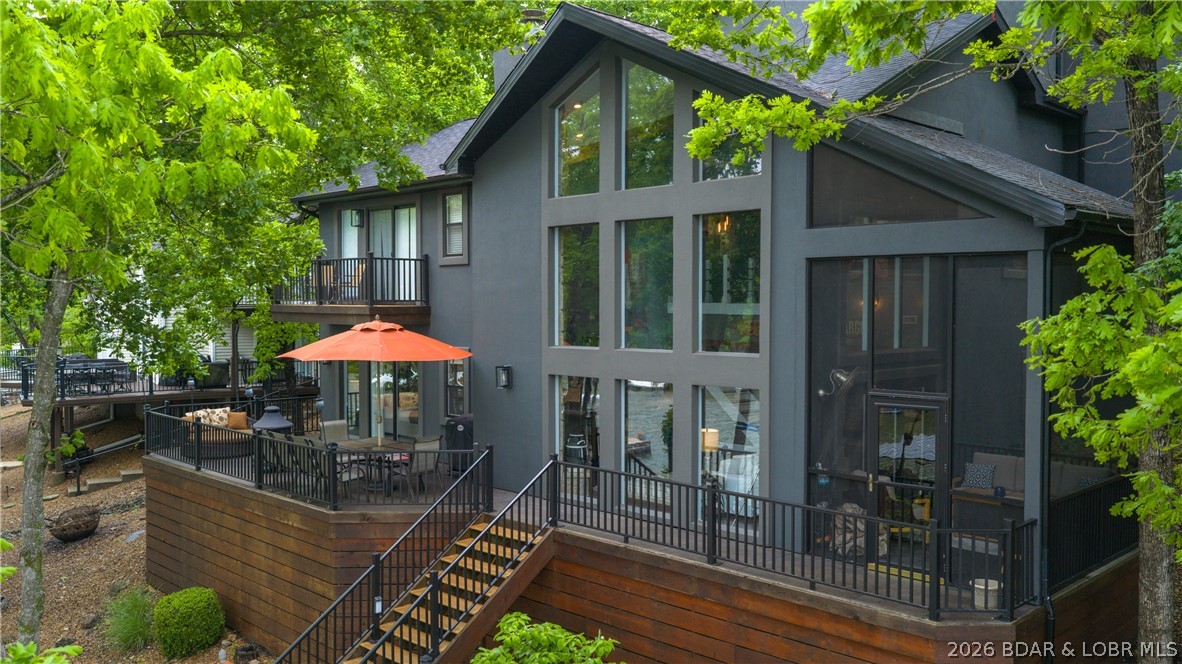 If you dream of the perfect lake lifestyle, this home is your answer! With comfortable sleeping space for 20 including 6 bedrooms (2 non-conforming) & a flat driveway for multiple vehicles, you will be a popular host. As you enter from the courtyard, you are greeted by a wall of lakeside windows which flood the interior with light & frame the spectacular lake views & mature landscaping perfectly. The natural stone fireplace, industrial lighting, & warm wood features along with casual decor throughout unite comfort and style. The kitchen functions perfectly with large butcher block island, white cabinets & counters, and open shelving. Multiple decks and a gentle sidewalk along a flowing water feature lead you to the main attraction--the lake! The custom concrete dock is every lake lover's dream with 2 boat slips, 2 covered PWC slips, & 2 large swim platforms. The no-wake cove is perfect for swimming, paddleboarding, kayaking or just floating, and when you need a break, come and enjoy your custom bar! The new dark gray exterior with bright orange and warm wood accents is the perfect blend of contemporary & rustic. Homes in this neighborhood do not come along often so don't wait!