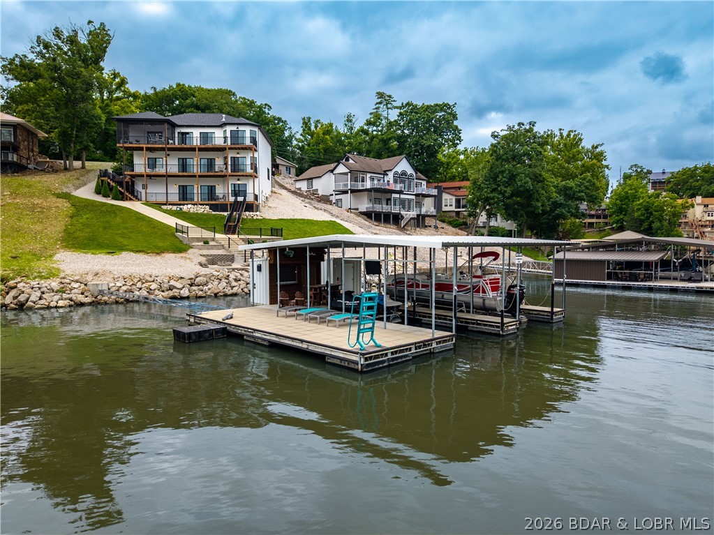 Luxury lakefront living in Blackhawk Estates! Built in 2020, this custom home offers 4,840 sq ft, 5 bedrooms, 5 bathrooms, and comes partially furnished and professionally decorated. Two bedrooms are en-suites, making it ideal for hosting family and guests. The home features soaring ceilings, spacious living areas, and a versatile third level with a half bath, kitchenette, and living space that could be a game room, bunk room, or the perfect hangout after a day on the lake. Main level living and a hot tub add to the convenience and enjoyment. Situated in a deep-water cove, the concrete dock is designed for entertaining with a swim platform, bar area, and both a 12x36 and 12x24 boat slip. A cart path makes getting to the dock effortless. Blackhawk Estates offers exceptional amenities including two community pools, pickle-ball courts, a playground, private marina, and private boat ramp. Located down HH, you're just minutes from golf, restaurants, and entertainment. This is more than a lake house—it's a complete Lake of the Ozarks lifestyle.