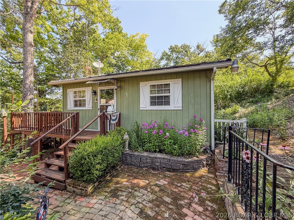 If you're looking for a peaceful cove setting, this furnished 2 bedroom, 1 bath is your own private sanctuary among the trees. The property offers 120 feet of lakefront with a 2 slips with hoists, swim platform, and waver runner lift, giving you the full lake package at an affordable price. The walk to the dock does include several steps, but it is softened by mature trees, brick courtyard-style walkways, flowers, a pavilion and peaceful outdoor spaces that make the setting feel charming and secluded.  Recent improvements include a roof approximately 3 years old, water heater approximately 1 year old, commercial-grade vinyl flooring, 220V power outside, GFI protection at the house and dock, new bunks on both dock lifts, and a 14-foot electric awning over the deck. An oversized garage and carport add great storage for lake toys, vehicles, and weekend gear. Appliances and most furnishings stay, making this an easy place to start enjoying lake life right away. Located close to marina, restaurant, and gas access. Come take a look and enjoy this summer at Lake of the Ozarks.