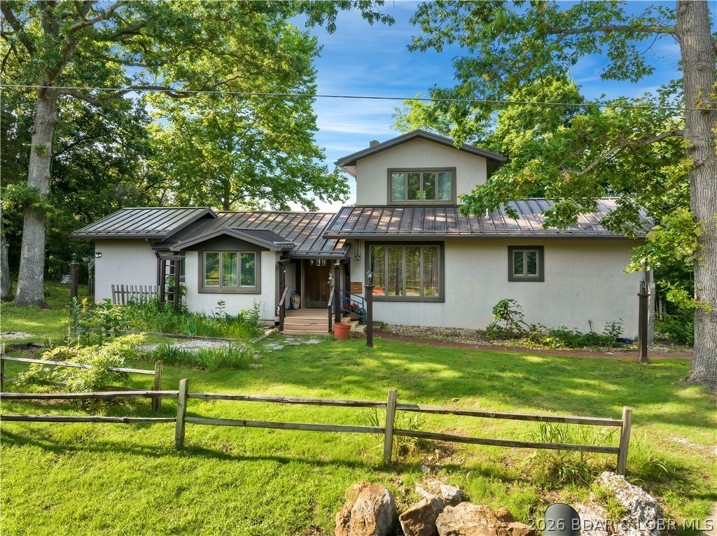 Not every lakefront property fits neatly into a box-and that is exactly what makes this one so memorable. 1.16 acres with 216’ of shoreline at the 5MM of the Little Niangua, 3-bedroom, 2-bath Lake of the Ozarks  delivers views, privacy, character, and creative energy from the moment you arrive. The home was designed with artistic influence throughout, featuring ornate light fixtures, wood and slate flooring, exposed beams, a wood stove, standing seam metal roof, and unique design elements around every corner. Large windows and multiple lake-facing spaces bring the outdoors in, while the lakeside wraparound deck offers room to relax, entertain, or simply take in the view. The primary suite includes deck access, a walk-in shower, jetted tub, and a spacious walk-in closet with built-in shelving. A detached 2-car garage for convenience, while the elevated detached retreat/studio, w/copper shingles, may be the most unforgettable part of the property — a separate creative space with dramatic lake views, perfect art studio, writing room, reading retreat, or peaceful guest overflow. With deep water and dockable shoreline, this is a rare opportunity to own a one-of-a-kind lakefront getaway.