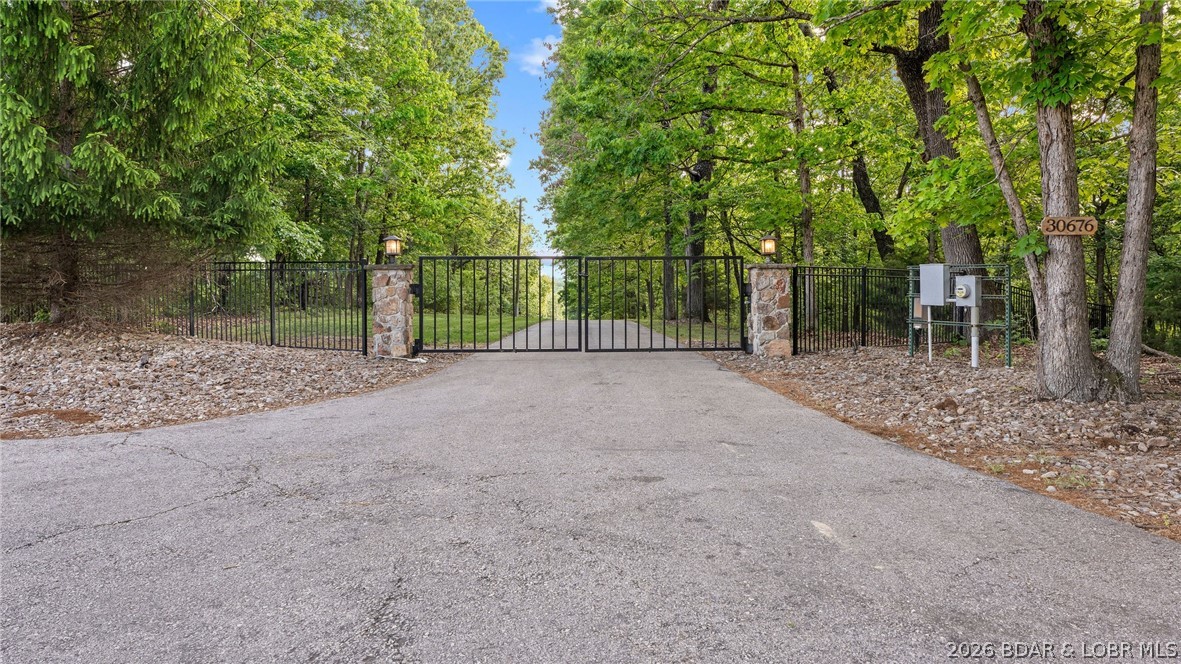 Welcome to 15 acres with over 400 feet of calm waterfront. This gated property offers space & privacy to enjoy every season. A 1,000 foot asphalt drive leads to a 40x60 insulated outbuilding with heated concrete floors, a bathroom, 12x40 carport, & an additional 12x20 storage area. The beautiful country style home offers 3 bedrooms, 2 baths, an open kitchen, heated Travertine floors, & a wet bar, designed for gathering with easy flow into the main living spaces. The kitchen is equipped with a Viking gas cooktop, & double ovens. Oak Tongue & Groove walls and beamed ceilings add warmth and character throughout. The master bedroom is an ensuite featuring a cozy fireplace, custom closet organizers, & a jetted tub in the bathroom. Large patios, an outdoor kitchen extend the living space outside, making it ideal for hosting. On the water, a two well dock includes a wet bar & swim platform & access to calm water ideal for relaxing. The grounds feature irrigated yard space and fire pits, giving you usable outdoor space throughout the year. Whether it is summer on the water or cooler months by the stone fireplace, this property offers flexibility for full time living or a private retreat.
