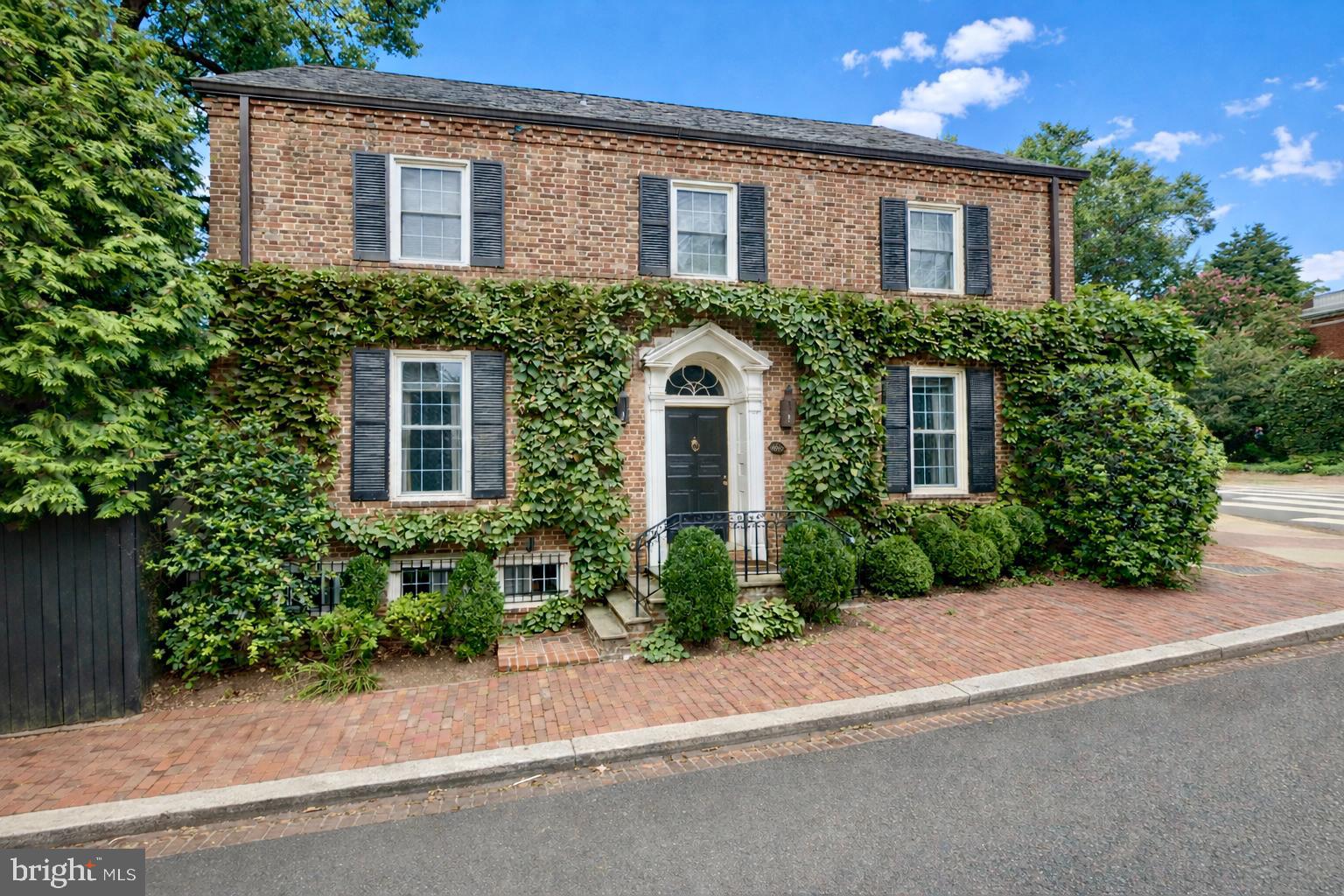 Well positioned on an expansive 6,000+ square foot private corner lot in the East Village of Georgetown, this distinguished residence presents an extraordinary opportunity to own a timeless home in Washington’s most sought-after location. Just steps from The Museum at Dumbarton Oaks, Montrose Park, and the celebrated boutiques and restaurants along Wisconsin Avenue, the property offers an unparalleled blend of tranquility and urban vibrancy.
The ivy-clad brick exterior exudes enduring elegance, accented by classic shutters and a stone staircase that ascends to the welcoming entry. Inside, a gracious foyer with a coat closet reveals beautifully preserved original hardwood floors and introduces the home’s refined architectural character.
The sun-drenched living room embodies timeless sophistication, featuring expansive windows, floor-to-ceiling built-in shelving, intricate crown molding, and a marble-surround fireplace with a carved wooden mantel. French doors open to the fully fenced south-facing rear garden and yard, an exceptionally private outdoor retreat framed by mature trees and lush landscaping.
The formal dining room mirrors the home’s bright disposition and detailed millwork, seamlessly connecting to a gourmet kitchen appointed with stainless steel appliances. Designed for effortless entertaining, the kitchen flows to an inviting outdoor dining area, creating an ideal setting for indoor-outdoor living and al fresco gatherings. A well-appointed butler’s pantry and powder room complete the main level.
Upstairs, the serene primary suite overlooks the verdant rear yard and features an additional fireplace, generous closet space, and a spacious bathroom with a soaking tub and frameless glass shower. Two additional sunlit bedrooms offer ample closet space and share the same refined detailing found throughout the home.
The finished third level, accessed by a pull-down ladder, offers a loft-like room for potential uses including a theatre, sitting room or office. The lower level offers over 1,100 square feet of space, presenting potential for a guest suite, recreation room and or gym. A detached one-car garage plus an additional surface parking space further enhance the property’s rare convenience.
Sited just off Montrose Park and moments from the storied gardens of The Museum at Dumbarton Oaks, this desirable address offers immediate access to some of Georgetown’s most treasured green spaces, ideal for morning walks, tennis, and tranquil afternoons beneath a canopy of trees. Just blocks away, the vibrant corridor of Wisconsin Avenue provides acclaimed dining, curated boutiques and neighborhood cafes. Move-in ready or offering outstanding potential for reimagination, 1698 32nd Street presents a compelling opportunity to secure a premier location with enduring appeal in the heart of Georgetown.