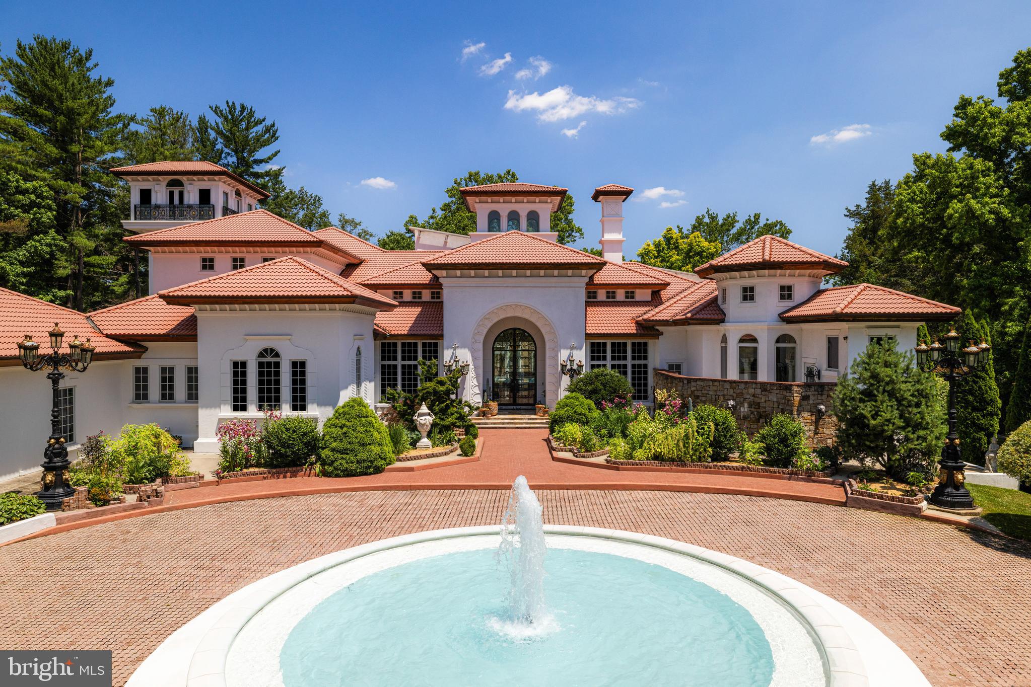 Casa de Amor, or “House of Love,” is a distinguished estate along Potomac’s prestigious Millionaire’s Mile. Set behind stately gates, the residence makes a striking first impression with its Spanish-style red-tile roof, graceful turrets, and a beautifully lit central fountain that draws the eye, especially at night. A paved motor court inspired by Mediterranean villas welcomes guests and leads to one of the Capital Region’s most memorable architectural facades.
 
Inside, custom arched glass and wrought iron doors open to a dramatic interior, where bold onyx floors, softly lit columns, and a carved marble fireplace establish the home’s refined aesthetic. With over 13,000 square feet of living space, the residence was thoughtfully designed using rare materials and timeless finishes throughout.
 
Natural light floods the soaring double-height dining room, while the formal living area showcases a full window wall overlooking the home’s signature feature, a stunning 50-foot indoor pool. Set beneath a glass roof reminiscent of those found in South Beach estates, the pool is surrounded by intricate tilework, palms, and vibrant accents that create a seamless indoor-outdoor feel usable year-round.
 
Nearly every room on the main level opens to the pool area, which also connects to a bright two-story entertaining space with its own commercial-grade kitchen. A dedicated pool bath includes a steam shower framed by detailed mosaics and decorative glasswork.
 
The primary suite offers privacy and comfort, featuring its own outdoor terrace, an expansive dressing room with multiple custom islands, and a spa-inspired bath clad in polished onyx. A richly finished library with dark wood paneling, gold leaf detailing, and a double-sided fireplace opens directly to the pool, as does the main-level wine cellar, a tasteful blend of stone, glass, and contemporary design.
 
More casual spaces include a breakfast room, a two-story great room, and a fully outfitted chef’s kitchen with custom cabinetry and Moroccan-inspired tile. Upstairs, a large sitting area connects to spacious secondary bedrooms, each with luxurious en-suite baths featuring deep soaking tubs and stone finishes.
 
A private glass elevator or spiral staircase leads to the home’s 53-foot observation tower, offering sweeping views across the property and surrounding area.
 
Outside, the grounds feature winding paths, ornate lanterns, and a secluded gazebo, bringing a sense of calm and beauty to the landscaped setting. Every detail has been thoughtfully considered, making Casa de Amor a rare and remarkable opportunity to own one of the region’s most unique and well-appointed residences.