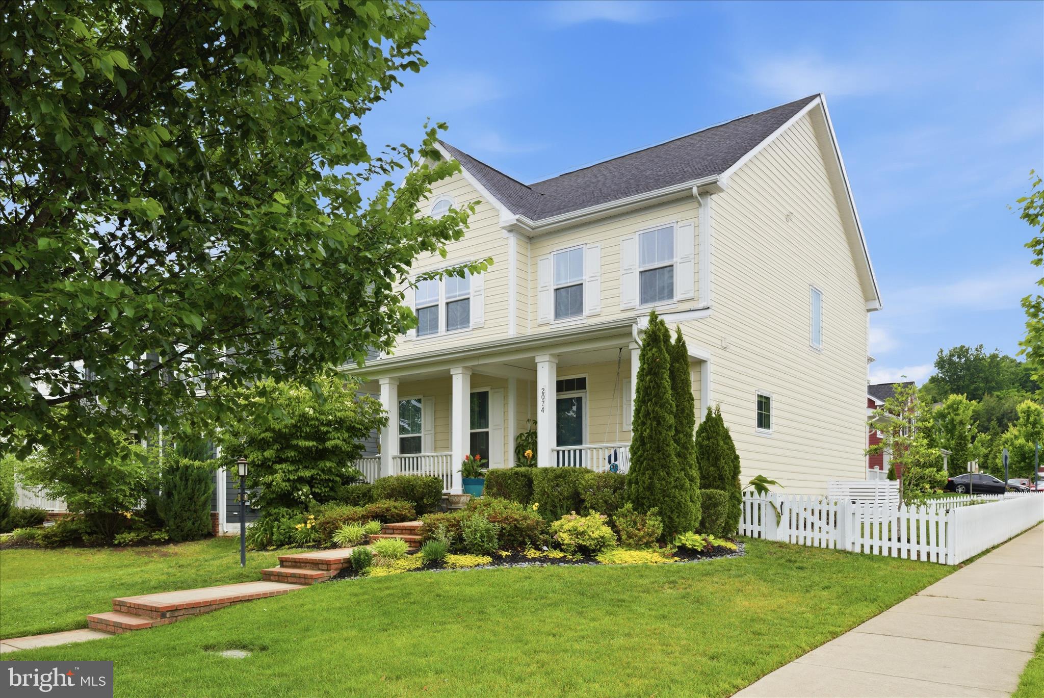 Welcome to 2074 River Heritage Boulevard — a beautifully appointed Craftsman-style home in the vibrant Potomac Shores community. Situated on a premium corner lot, this exceptional residence combines timeless curb appeal with modern luxury and one of the community’s most versatile floor plans.

From the charming soft-yellow exterior and white picket fence to the inviting full front porch, this home makes a memorable first impression. Inside, nearly 4,000 square feet of thoughtfully designed living space offers 5 bedrooms, 4.5 baths, and flexible spaces perfectly suited for today’s lifestyle.

A standout feature is the rare secondary private suite above the garage, complete with its own staircase, en suite bath, and walk-in closet — ideal for multigenerational living, guests, an au pair, or a private home office retreat.

The main level is designed for both everyday comfort and effortless entertaining, featuring hardwood floors, 9-foot ceilings, a formal dining room with coffered ceiling, and an open-concept family room anchored by a cozy fireplace. The gourmet kitchen impresses with granite countertops, a large center island, stainless steel appliances, custom backsplash, pantry, and spacious breakfast area.

Upstairs, the luxurious primary suite offers dual oversized walk-in closets and a spa-inspired bathroom with double vanities, walk-in shower, and private water closet. Three additional generously sized bedrooms, a full hall bath, and upper-level laundry complete the upper floor.

The finished lower level expands the home’s entertainment potential with luxury vinyl plank flooring, a full bath, wet bar and ample gathering space for movie nights, game days, or hosting guests.

Outdoor living is equally inviting with a private side deck, fenced yard, mature landscaping, and in-ground irrigation system.

Located in the award-winning Potomac Shores community, residents enjoy resort-style amenities including pools, a new upgraded fitness center, miles of trails, golf course access, sports fields, high speed internet, and less than 2 miles from the future VRE commuter rail access. Conveniently located near I-95, Route 1, Stonebridge Town Center, Potomac Mills, dining, shopping, and top-rated schools.

This is more than a home — it’s a lifestyle.