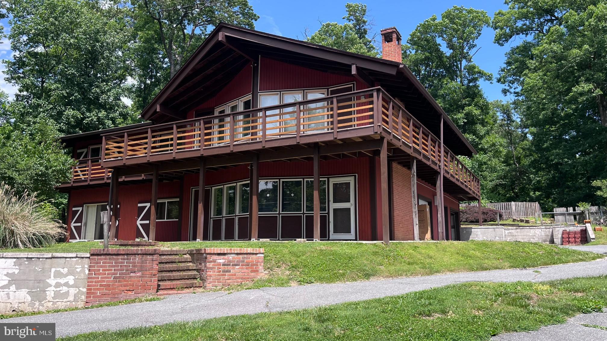Tucked high among the wooded ridgelines of Braddock Heights, this distinctive lodge-inspired home offers a rare combination of architectural character, privacy, and convenience just minutes from downtown Frederick. Established, elevated, and quietly tucked into a mature landscape setting, the property feels more like a private retreat than a typical suburban home.

Designed in the early 1970s with dramatic exposed timber beams, soaring cathedral ceilings, and expansive walls of glass, the home has been thoughtfully refreshed over time while preserving the warmth and authenticity of its original design. A large wraparound deck extends the living space outdoors, creating the perfect setting for morning coffee, evening gatherings, or simply enjoying the surrounding woodland views.

The heart of the home is a stunning sunken great room featuring floor-to-ceiling windows, a wet bar, ceramic tile flooring, and an extraordinary beam-framed cathedral ceiling that creates an immediate sense of openness and character. Throughout the home, unique architectural details and carefully preserved original elements provide a level of craftsmanship and personality that is increasingly difficult to find.

The kitchen has been carefully rejuvenated with updated appliances, fixtures, and extensive storage while remaining true to the home's architectural style. Bright and welcoming, it enjoys walls of windows overlooking the backyard and offers direct access to two adjoining dining spaces. A striking three-sided brick fireplace with copper detailing serves as the centerpiece of the informal dining area while adding warmth and ambiance throughout the main living spaces.

The main level includes three bedrooms, including a spacious primary suite featuring a large sleeping area, an oversized dressing room, and a private bath with vanity. Vaulted ceilings, distinctive windows, and thoughtful architectural touches continue throughout the bedroom wing, creating a cohesive and inviting atmosphere.

The finished lower level offers exceptional flexibility with two additional bedrooms, a large family room, generous laundry and utility areas, abundant storage, and direct access to the oversized two-car garage. An additional workshop or storage bay provides valuable space for hobbies, projects, outdoor equipment, or seasonal storage.

Outside, the three-quarter-acre property blends mature native trees with established landscaping to create a setting that feels peaceful, private, and naturally integrated into its surroundings. Whether entertaining friends, working from home, commuting to Washington, or simply seeking a home with warmth and character, this property offers a lifestyle that is increasingly hard to find.

Conveniently located near downtown Frederick, commuter routes including US-15, US-340, I-70, I-270, MARC rail service, shopping, dining, and outdoor recreation.

Existing fenced in-ground pool currently inactive and conveys as-is. The pool structure, cover, fencing, and equipment are present, offering future owners the opportunity to restore, redesign, or repurpose the space according to their vision.

This is not a cookie-cutter home. It is a thoughtfully preserved architectural property with warmth, scale, flexibility, and personality.  For buyers who appreciate distinctive design. natural surroundings, and the rewards of owning a home with true character, 5605 Jefferson offers a lifestyle the is increasingly difficult to find.