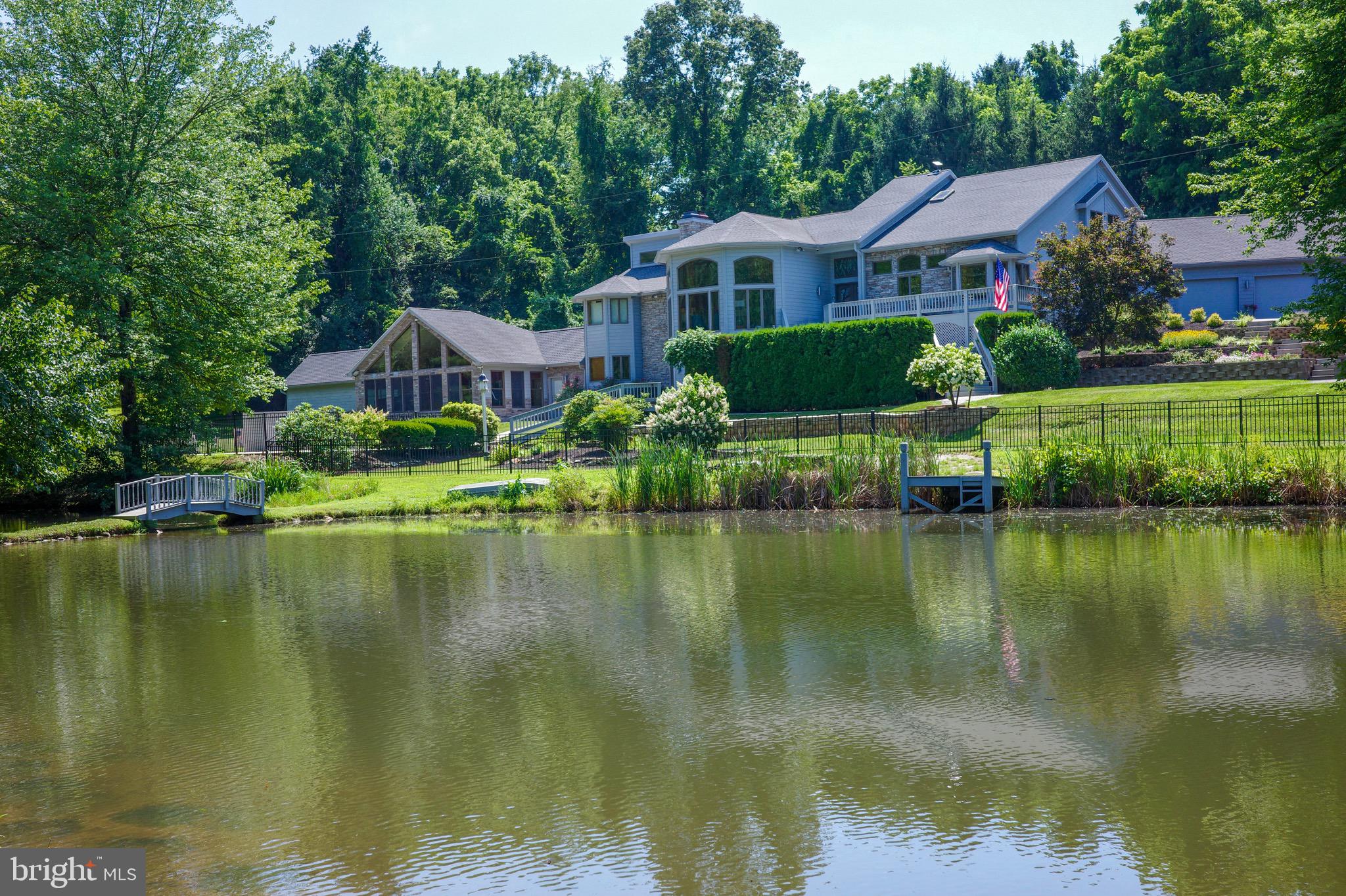 Stunning 7,706 square foot custom, secluded estate on 15.09 acres at the end of a pipe stem in the Red Lion schools less than 10 minutes from I-83 and route 30! This tucked away resort was built in 1992 by Larry Anderson for himself with 2”x6” exterior construction and features an over 2,100 square foot addition from 2008. Situated privately at the end of the street, the property features 3 large spring-fed ponds stocked with catfish, bass and sunnies, including a functional waterfall, an in-ground pool, and an expansive multi-level deck overlooking the water. The home welcomes you with beautiful nature-inspired stained glass in the front door. Artistic touches continue throughout the home, highlighted by a unique tree stump sink in the powder room. The gourmet kitchen is a true showpiece featuring a large island topped in rare Blue Bahia granite from Brazil, a six-burner Viking gas cooktop with pot filler, and a professional three-bowl stainless steel sink with foot pedal operation. It also includes a Jenn-Air
refrigerator and striking, colorful angled and vaulted ceilings. The main level also features a spacious primary suite with two large walk-in closets featuring professionally installed organizers. The luxurious primary bathroom includes a Jacuzzi soaking tub, a beautiful stone shower with two ceiling-mounted rain shower heads, and two hand wands. A convenient mudroom and laundry room complete the main level with the LG washer and dryer staying with the home, plus a functional laundry chute. This exceptional home features two separate HVAC and two central air units and 3 water heaters. The roof was replaced just 5 years ago. The exterior is finished in cedar and manufactured stone, is professionally landscaped and includes an extensive security system with PTZ cameras. The dramatic sunken library on the lower level is wrapped floor-to-ceiling in exquisite handcrafted white oak raised paneling with built-ins and bookshelves. The lower level is an entertainer’s dream, highlighted by a spectacular 16-seat, multi-level home theater installed by Dick Baker of Audio Visual Contractors of York, featuring a Sony 4K SXRD projector an 11-foot diagonal screen, 12 leather electric recliners plus 4 bar stools, custom lighted alcoves perfect for displaying memorabilia and remote-controlled lighting. Garage enthusiasts will be amazed by the parking capacity. There is an oversized attached three-car garage that can easily fit four vehicles, plus floored storage above the garage, a detached two-car garage, and an additional one-car garage. This gives the home true 6 -7 car capacity plus a Tesla wall charger for electric vehicles. The property is beautifully wooded with approximately 12 acres of woods & is teeming with wildlife. Deer, fox, geese and a variety of birds are regular visitors to this peaceful, secluded setting. Living here truly feels like having your own private resort. Call today to schedule your private showing and step through — a whole new world awaits.