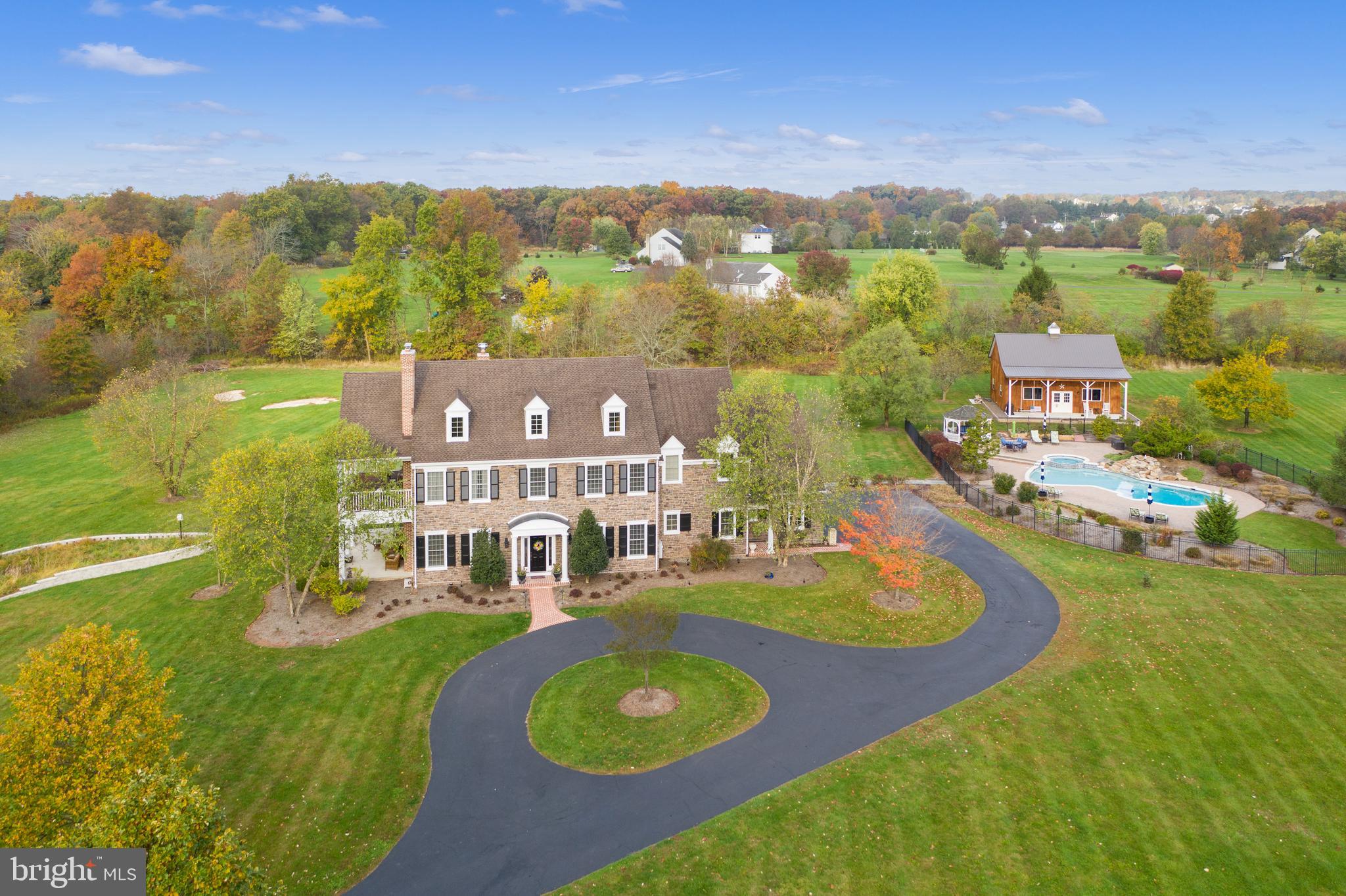 Set back on a quiet country road and surrounded by nearly 6 acres of bucolic landscape, this custom built estate blends refined craftsmanship with exceptional indoor–outdoor living. A winding, tree lined drive framed by stone walls leads to a circular driveway and a striking stone and Hardie Plank façade. A covered front porch opens into a gracious foyer with random width hardwood floors and 10' ceilings that span the entire first level. To the left, a formal living room with gas fireplace connects through French doors to a spacious study/home office and a 32' x 12' covered side porch. Ideal for outdoor dining or a peaceful work from home retreat. To the right of the foyer, French doors reveal an elegant dining room featuring a tray ceiling, custom millwork, wainscoting and a wet bar accented by a beautiful stone wall.
A barrel vaulted hallway leads to the stunning great room, complete with coffered ceiling, wood burning stone fireplace, architectural columns and an expansive window seat with storage. The open layout flows seamlessly into the gourmet kitchen, showcasing a large granite island, soapstone countertops, handcrafted inlay cabinetry, stainless steel appliances, a BlueStar 6 burner range with hood, second wall oven, warming drawer, Sub Zero refrigerator and central vac with baseboard sweep inlet. The cathedral ceiling breakfast room opens to a slate patio perfect for dining and lounging.
The first floor also includes a walk in pantry, mudroom with side entrance, two powder rooms, a second home office and an oversized 3 car garage with refinished Signature Flake epoxy flooring by Garage Kings.
Upstairs, the luxurious primary suite features a tray ceiling, gas fireplace, two custom walk-in closets, and a spa like bath with dual vanities, soaking tub, stall shower and private water closet. A private 32' x 12' mahogany covered porch overlooks the expansive backyard, including your own par 3 golf hole. Three additional bedrooms with generous closets, two full baths, a third office area and a laundry room complete the second floor.
The third floor offers an additional 1,227 sq ft with high ceilings, dormers, electric and roughed in plumbing for future additional living space. The lower level provides a full entertainment suite: family room with fireplace, wet bar, game area, gym with commercial rubber flooring, full bath with a sauna and changing room and extensive storage with space for a future wine cellar.
Step outside to the impressive pool complex featuring a cascading waterfall, hot tub and gazebo. Overlooking the pool is fantastic Amish built pole barn with a covered porch and swings. Perfect for hobbyists, collectors, entertaining or use as a pool house.
This exceptional property offers unmatched flexibility with three home office spaces, multiple covered porches and expansive patios—ideal for both relaxation and entertaining. Recent updates include a newer roof (2020), pool resurfacing with quartz finish (2019) and Pole Barn (2019). 
Conveniently located minutes from charming Skippack Village, the PA Turnpike Northeast Extension, and an easy drive to Philadelphia, Plymouth Meeting and King of Prussia. Outdoor enthusiasts will appreciate proximity to Evansburg State Park, Valley Forge National Park, local golf courses, and winter skiing at Spring Mountain.