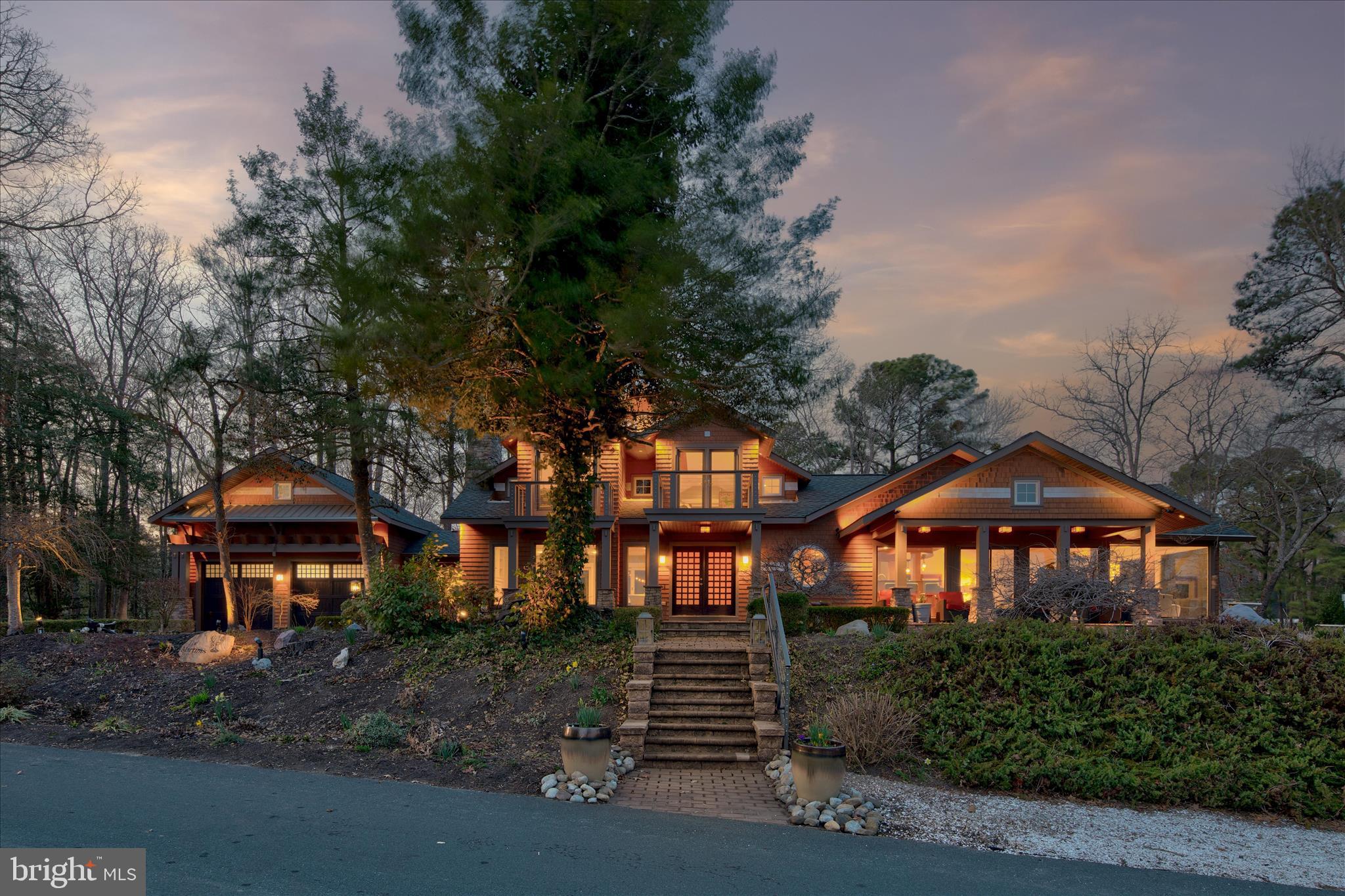 A One-of-a-Kind Waterfront Sanctuary on the Peninsula of Piney Island

Truly one of a kind, this remarkable custom residence is gracefully tucked away on the secluded peninsula of Piney Island. Welcome to 10931 Piney Island Drive, redesigned and rebuilt in 2012,  where architecture, nature, and water converge to create an extraordinary coastal sanctuary. From the moment it comes into view, the home feels as though it has always belonged to this peaceful landscape. Cloaked in natural cedar shake siding and thoughtfully designed to blend with its wooded surroundings, the residence reflects a harmonious fusion of Craftsman, Asian, and classic Shingle-style architecture, elevated with clean modern lines and expansive glass.
Perched in a regal position above the surrounding waterways, the home captures breathtaking panoramic views of Shingle Landing Prong and Perkins Creek. Here, the ever-changing light dances across the water, and the scenic waterways invite endless exploration, leading adventurous boaters all the way to the Atlantic Ocean. Inside, architectural artistry and refined craftsmanship take center stage. Walls of glass frame the spectacular natural surroundings, filling the home with light while blurring the boundary between indoors and out. Thoughtfully designed spaces, rich architectural details, and carefully curated finishes create interiors that rival the beauty of the landscape beyond. The kitchen has been beautifully refreshed in 2025 with new appliances including a refrigerator/freezer, dishwasher, wine cooler, and refrigerated drawers, creating a well-appointed culinary hub perfect for entertaining. Throughout the home, tray ceilings with ambient lighting add elegance to the bedrooms, dining room, and foyer, while unique features such as a dedicated humidor and a striking 75-gallon aquarium reflect the home’s custom character.
Outdoor living here is nothing short of exceptional. Multiple decks, including three on the second level, offer private vantage points for soaking in the sweeping water views. Gather around the gas fire pit, enjoy the warmth of the outdoor fireplace while watching the game on the patio television, or relax on the welcoming front porch. The porch off the kitchen is perfect for grilling, making alfresco dining effortless.
The grounds themselves feel like a private retreat, enhanced by two serene ponds, a gentle stream, and elegant rain chains that guide water into tranquil garden features. A waterfall and fountain create a peaceful backdrop to the rear patio, while perennial gardens cascade naturally along the waterfront bank.
Boating and waterfront recreation are easily enjoyed from the private dock, which features a 12,000 pound boat lift, fish cutting station, and illuminated post for evening returns from the water. Recent improvements further enhance the home’s comfort and efficiency, including a new geothermal HVAC system in 2024, a renovated primary bath with updated flooring, tile, and fixtures, refreshed interior paint, updated flooring in the primary bedroom, and an upgraded hall bath. A whole-house generator, water treatment system, alarm system, and thoughtfully integrated multi-zone audio system provide modern convenience and peace of mind. The lower-level Utility/Storage room offers abundant space for all of your outdoor gear. There is a oversized 2-car garage with a walk-up to an additional room, perfect for an office and offers more storage options.
Private, refined, and surrounded by breathtaking natural beauty, 10931 Piney Island Drive is more than a home, it is a waterfront retreat designed for living, gathering, and experiencing the very best of coastal life.