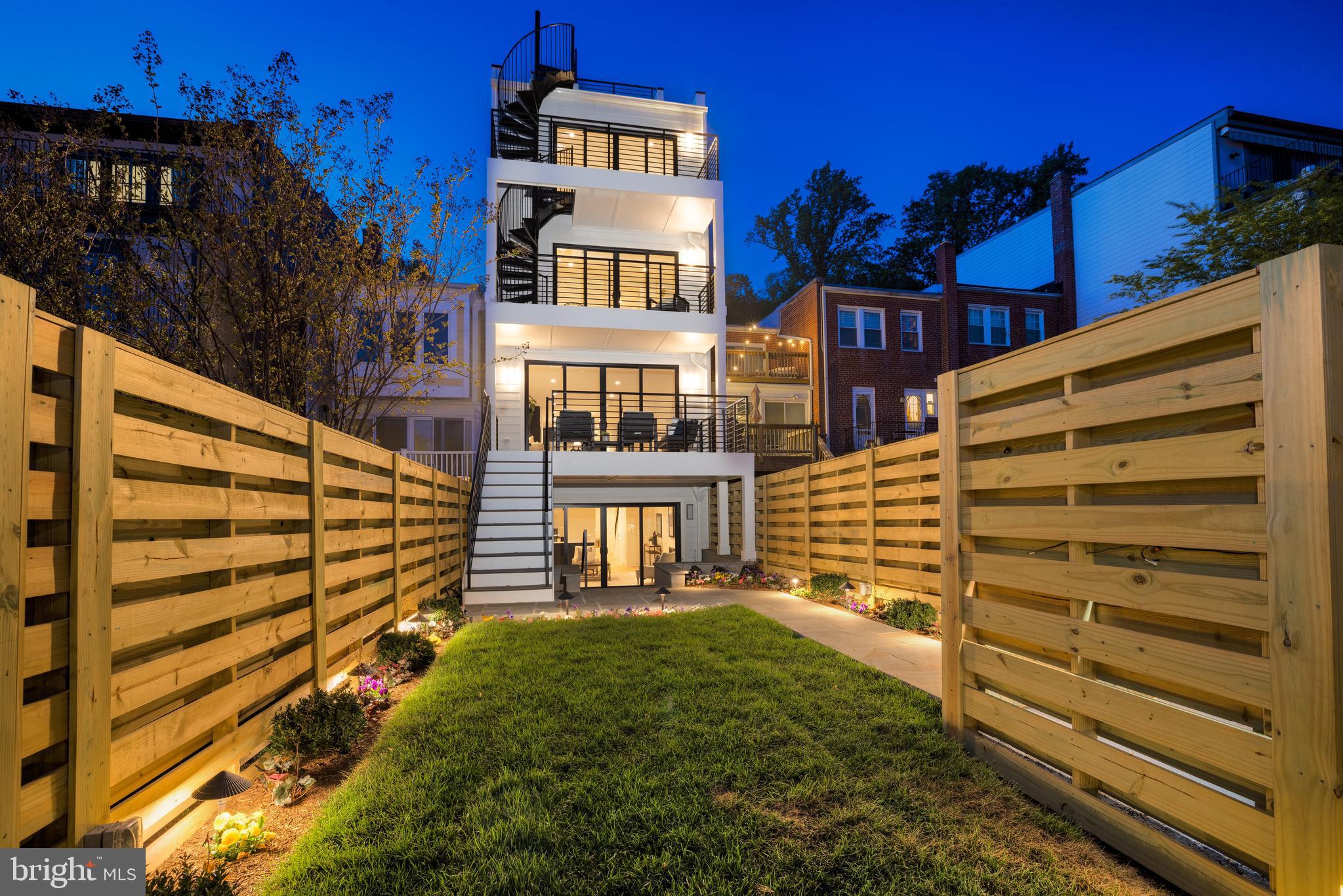 With more than 4,000 square feet, this newly constructed five-bedroom, five-and-half-bathroom home boasts a stunning, contemporary design with a distinctive white brick exterior. The high-end finishes, refined design elements and high-quality craftsmanship continue in the interior with floor-to-ceiling windows, a spacious gourmet kitchen and large living spaces. Enjoy gorgeous views from the rooftop deck, as well as a spacious rear yard and multiple balconies. The rear parking pad provides off-street parking for two cars. This is a rare opportunity to own a truly exceptional property.
Owners will delight in welcoming guests through the foyer into a beautifully designed main living area. A splendid gourmet kitchen features a full suite of upgraded stainless-steel Viking appliances including a 48-inch gas range with grill and a custom hood, a 30-inch built-in column refrigerator, a 30-inch built-in column freezer with ice maker, and an under-counter drawer microwave, dishwasher and beverage refrigerator. Calcutta Miraggio quartz countertops, backsplash and 12.5-foot kitchen island with waterfall sides complement the custom cabinetry, complete with a coffee bar/appliance garage. Additional storage is built-in with a custom pantry. The kitchen flows into the dining and living rooms. A Real Flame Corretto 72-inch-wide wall-mounted vent-free electric fireplace creates the perfect focal point for the living room. A wall of glass doors open to the rear deck and garden, creating an open flow for everyday living and entertaining. The front of the main level offers function and convenience with an office/flex space that overlooks the front garden, powder room, and spacious closet for housing outdoor attire.  
The third level boasts two generously sized bedroom suites with extensive closets and large bathrooms. The front bedroom suite overlooks the park with two sets of large casement windows. The private ensuite bath includes a walk-in closet and Architessa porcelain tile flooring and accent wall. The rear bedroom provides ample storage space with double closets, as well as a private entrance to the adjacent full bathroom, completed with Architessa porcelain tile. Owners will enjoy relaxing on the private balcony or taking the spiral stairs up to the roofdeck with gorgeous treetop views of the District. Centered between the two bedroom suites sits a multipurpose flex room that could be a media room, possible guest bedroom, or exercise/spa room.
The lower level is beautifully designed with both function and style in mind. Generously proportioned, the family room is built for entertaining. An elegant 72-inch wall-mounted vent-free fireplace creates the perfect focal point while glass doors provide open flow to the covered blue-stone terrace and rear garden. At the front of the lower level, the fifth bedroom features double closets and a private entrance to the adjacent full bathroom, creating the perfect guest suite. Everyday function and convenience is achieved with the large laundry/utility room designed with a dog-washing station. A flex room could be used as a mudroom, storage, wine room, etc.