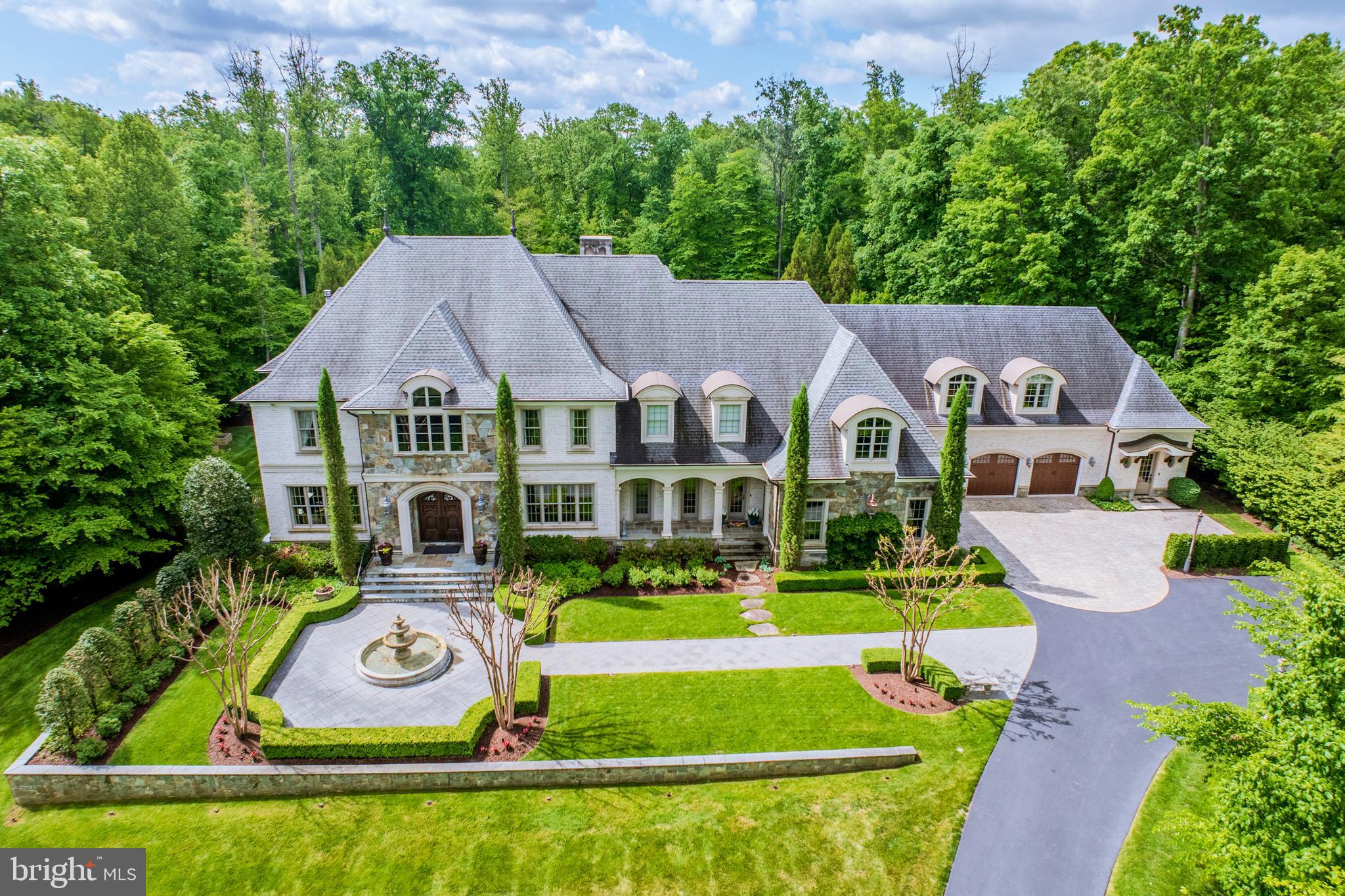 A masterful expression of French château-inspired elegance, this extraordinary estate is a private sanctuary where timeless architecture, resort-style living, and refined craftsmanship converge across 5.16 breathtaking acres in the heart of Grenata. Beyond stately gas lanterns and a flowing fountain, a picturesque arrival unfolds through lush woodland surroundings, a refined breezeway, and a hand-carved entry that sets the tone for the remarkable experience within. Spanning over 11,500 square feet, the residence is thoughtfully curated with bespoke millwork, rich hardwoods, soaring coffered ceilings, and the quiet luxury of geothermal comfort throughout. Designed for both grand entertaining and intimate everyday living, the interiors offer an effortless blend of sophistication and warmth. A dramatic floating staircase serves as the architectural centerpiece, while elegant gathering spaces illuminated by sparkling chandeliers invite conversation, music, and unforgettable evenings by the dual-sided fireplace. At the heart of the home, the chef’s kitchen is both functional and exquisite — featuring custom cabinetry, professional-grade appliances, intricate detailing, and a fully appointed butler’s pantry. Adjacent indoor and outdoor living spaces create a seamless entertaining experience, extending onto an enclosed deck complete with retractable screens, an outdoor kitchen, and a fireside lounge overlooking the estate grounds.The resort-caliber pool setting serves as the crown jewel of the property, offering sun-drenched  relaxation alongside a beautifully concealed winding waterslide that brings an element of playful luxury to the serene landscape. A dedicated pool bath with double showers enhances the experience, while the expansive lower level was designed for elevated entertaining — complete with spaces for wine tastings, game nights, cinematic screenings, catered gatherings, and a striking custom bar designed for effortless hosting. Four tranquil bedroom suites each offer private en suite baths, including a spectacular primary retreat with dual bespoke dressing rooms and a spa-inspired steam shower sanctuary. Additional flexible living spaces include a dedicated upper-level executive office suite complete with a private entrance and welcoming lobby, creating an exceptional environment for private consultations, remote business operations, wellness services, or inspired creative pursuits. A separate home gym and main-level bonus suite with full bath further enhance the estate’s versatility and lifestyle appeal. Further highlights include a Victorian-style conservatory greenhouse, spacious mudroom, and attached four-car garage. Perfectly positioned moments from shopping, dining, wineries, and the equestrian lifestyle of Leesburg’s celebrated Hunt and Wine Country, this exceptional estate delivers an unparalleled luxury lifestyle defined by privacy, beauty, and timeless distinction.