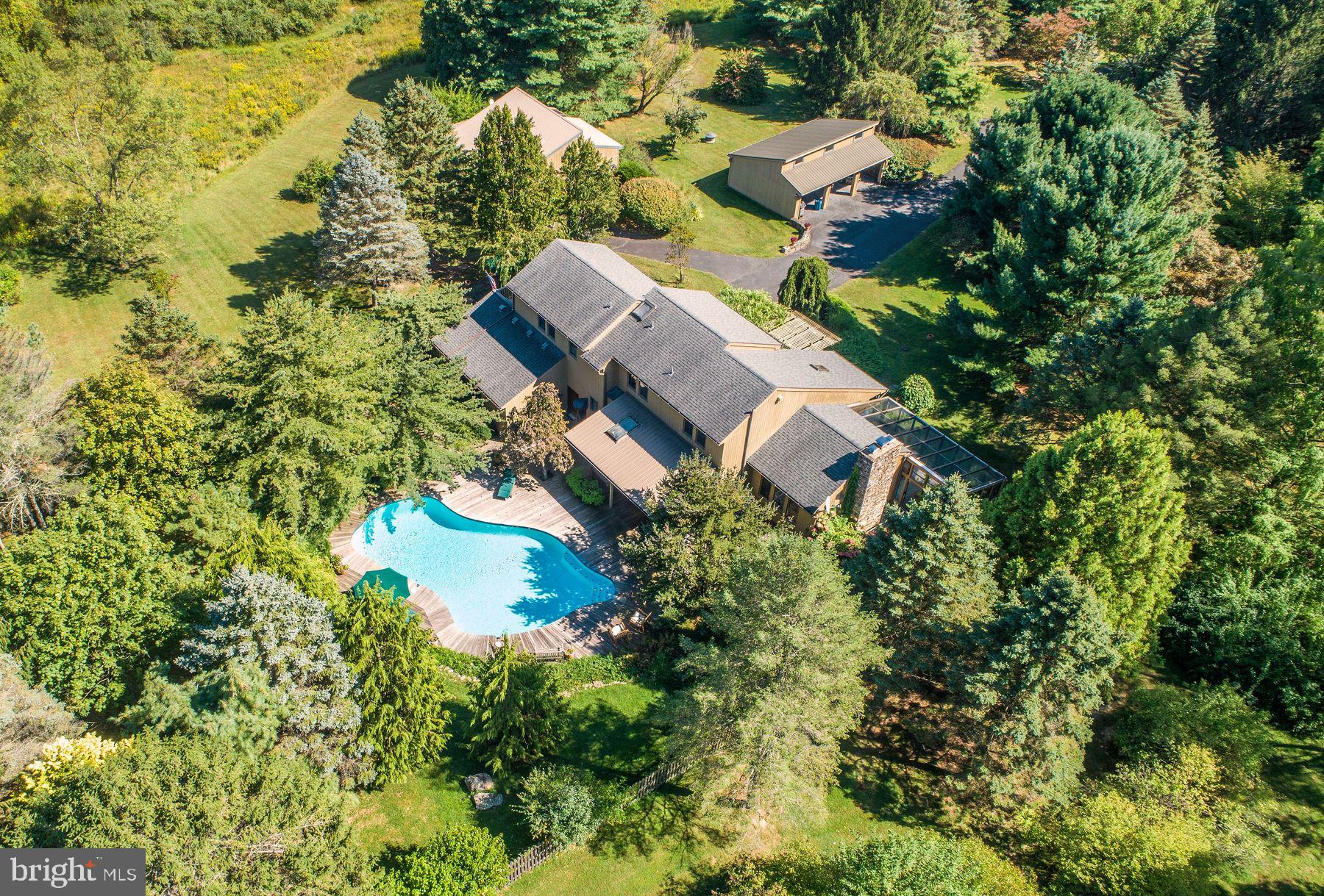 Tucked away and situated on over 9 acres in Springfield Township, one of the best-preserved and scenic areas of Bucks County, this stunning 4-bedroom contemporary home is a rare offering. Designed with an eye for quality and detail, it blends custom cedar, stone and glasswork in a way that celebrates both craftsmanship and nature. Walls of glass and thoughtfully designed spaces allow natural light to pour into every corner, creating interiors that feel both expansive and inviting. The setting is nothing short of idyllic. Surrounded by rolling fields and mature trees, the property offers panoramic views. At night, the skies open to breathtaking stargazing-an unmatched backdrop of peace that feels worlds away from every day. Outdoor living is equally captivating with an inground swimming pool bordered in ceramic tile and framed by specimen plantings and mature landscaping that create a private oasis for warm-weather enjoyment. Entertaining is effortless on the main level, beginning with the large dining room that sets the stage for memorable gatherings. Just a few steps down, a spacious family room opens directly to the stone terrace, creating a seamless connection between indoor comfort and outdoor living. The gourmet kitchen is just steps away, offering every convenience a host could desire from its Wolf six-burner range with griddle and double ovens to the suite of Sub-Zero appliances, all framed by granite countertops and limestone flooring. The flow continues into the living room, where a dramatic floor-to-ceiling stone fireplace creates a warm focal point and a French door opens to the sun-filled solarium with a hot tub, offering a serene space for year-round relaxation.  A first-floor guest bedroom suite ensures privacy and comfort for overnight visitors. Upstairs, the primary suite serves as a private retreat, featuring its own balcony overlooking the beautifully landscaped grounds and specimen plantings. Two additional bedrooms and a hall bath complete this level.  A versatile detached studio expands the property's possibilities, offering heat, water and abundant natural light.  This space includes a loft, a dedicated office or workout room and an adjoining greenhouse- creating an inspiring setting for art, wellness or work- all surrounded by the serenity of nature.   A 3-bay carport provides the perfect finishing touch to this country retreat. This is more than a home- it is a sanctuary where modern comforts meet natural beauty, offering privacy, sophistication and a lifestyle that celebrates the very best of country living.