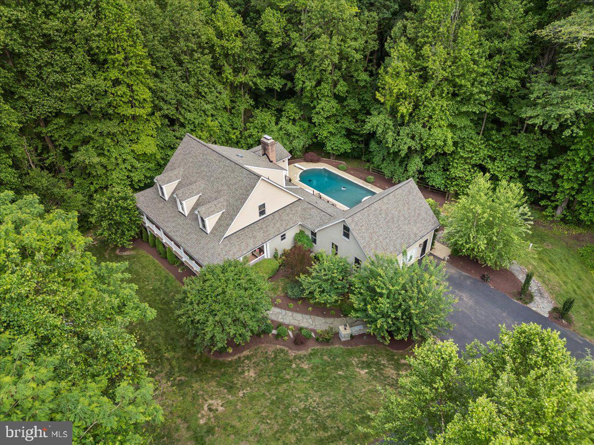 Over 5,000 finished square feet of luxury living featuring a chef’s kitchen with a premium Wolf stove, a heated saltwater pool with spa, and exceptional spaces for entertainment, all nestled in a private, wooded setting less than an hour from Washington, D.C. and Annapolis. The impressive kitchen is the heart of the home, offering a premium Wolf stove, abundant workspace, and an open layout that flows seamlessly into the main living areas, where soaring vaulted ceilings, refinished hardwood flooring, custom built-ins, carved wood ceilings, and a cozy fireplace showcase the home’s quality craftsmanship and timeless design. The main level offers a spacious primary suite with a full bath, plus an additional full bath for guests. Upstairs are three additional bedrooms, including a private en-suite and a charming bedroom with a hand-painted forest mural. Need flexible living space? The finished detached garage includes a dedicated studio/workspace and a private guest suite with a bedroom, full bath, and separate work area—perfect for extended family, overnight guests, a home office, or creative pursuits. The recently finished lower level adds even more versatility with a bedroom, expansive recreation or fitness room, and a half bath with direct access to the backyard. Outside, your private retreat awaits with a 4-year-old heated saltwater pool featuring a PebbleTec finish, built-in spa, color-changing lighting, and extensive landscape lighting that creates a spectacular setting for evening entertaining. Ample parking and a large storage building add everyday convenience. Meticulously maintained and thoughtfully updated throughout, this one-of-a-kind property offers the perfect blend of luxury, privacy, versatility, and convenience.