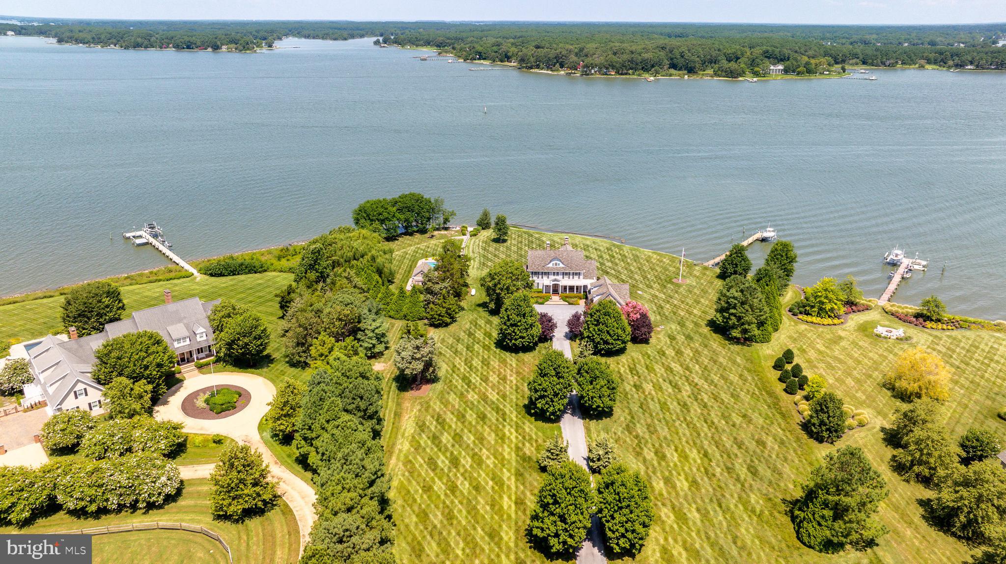 First time offering in Morgans Point. Custom built estate designed by architect Lauren Dianich of Atelier 11, this elegant Georgian-style brick and shingle residence offers over 5,200± square feet of thoughtfully designed living space filled with natural light and panoramic water views of the Tred Avon River. Set on 5± acres, the home is crafted for both refined entertaining and private, relaxed waterfront living. The heart of the home is the River Room, surrounded by windows that frame sweeping views of the Tred Avon River. Hardwood floors by Universal Floors in D.C. feature an inlaid compass medallion that points to magnetic north, creating a distinctive focal point. A fireplace anchors the space, with a screened-in porch with its own fireplace just beyond, perfect for enjoying chilly evenings. The chef’s kitchen is equipped with professional-grade appliances including a Wolf range and double wall ovens, Sub-Zero refrigerator, Asko full-size dishwasher, and Fisher & Paykel dishwasher drawers. A large island offers a wine fridge and illuminated display cabinetry, while the butler’s pantry—complete with an additional refrigerator and charming porthole windows framing water views—enhances the home’s functionality. Additionally, a custom-built oval wet bar with a two-drawer Sub-Zero refrigerator offers substantial cabinetry. This space provides a natural gathering point for entertaining. A large mudroom with powder room provides convenience for busy households. Also on the main level are a library with floor-to-ceiling shelving and a wood-burning fireplace, a fitness room with water vistas, a formal half-bath, and a first-floor en-suite bedroom ideal for guests. A dedicated utility entrance allows for discreet service and maintenance without entering the main living spaces. A 25kW standby generator provides reliable backup power for the main residence, offering peace of mind during outages. Upstairs, the primary suite with a gas fireplace serves as a retreat, with its spacious bathroom offering a shower, jetted soaking tub, and two walk-in closets—one with its own half-bath. Additional bedrooms include an upper-level en-suite and family-friendly accommodations, all supported by a conveniently located laundry room. Completing this floor is a private office with a gas fireplace and panoramic river views, offering an inspiring space for work or study. A generously sized, detached three-car garage includes a second-floor guest quarters with a kitchenette, washer and dryer, and en-suite bedroom, where windows capture tranquil water views. Outdoors, enjoy resort-like amenities including a heated pool with a fully retractable cover and a pool pavilion with its own bathroom and outdoor shower. The grounds are beautifully landscaped and designed for relaxation, with serene river views visible from nearly every room of the property. This rare offering seamlessly blends architectural pedigree, modern luxury, and a spectacular setting on the Tred Avon River—an exceptional opportunity to experience Eastern Shore living at its finest.