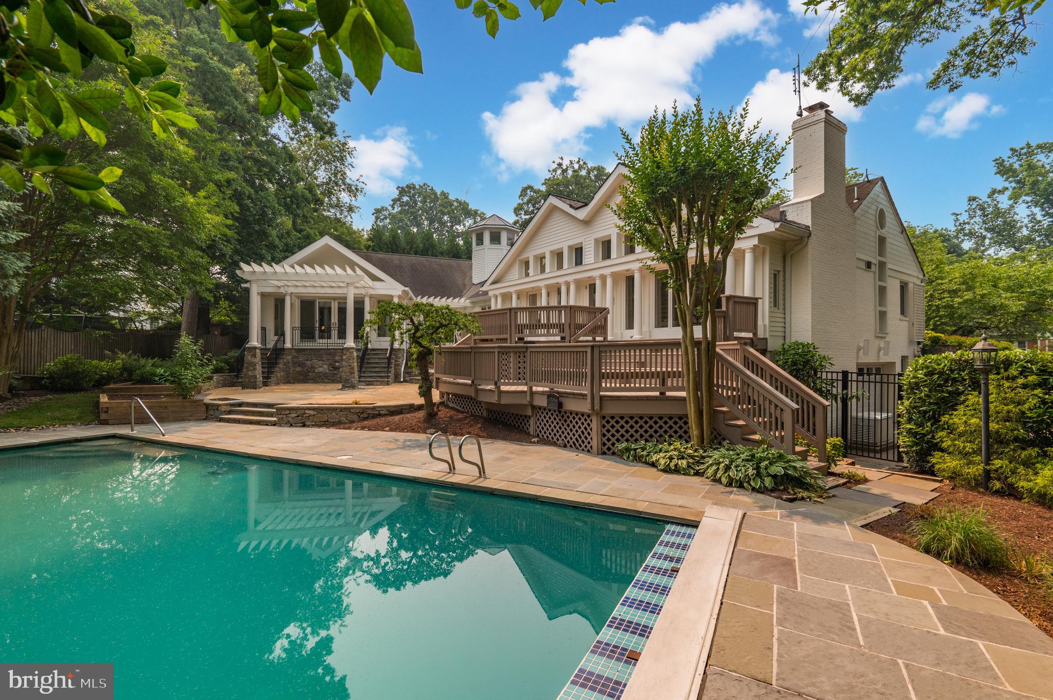 Sited on a quiet cul-de-sac along a Cherry Blossom lined street, 5807 Hillburne Way is a uniquely appointed and meticulously maintained, custom-built home offering unparalleled Main Level living in Chevy Chase’s coveted Kenwood neighborhood. Beautifully manicured gardens span the level 0.35 acre property and encompass the residence’s idyllic outdoor decks and patios overlooking a sprawling 40’ heated swimming pool, to offer outdoor amenities that exquisitely complement the home’s interiors. Boasting 3 Bedrooms and 3.5 Bathrooms across 10,400 square feet and 3 levels, this customized showpiece displays thoughtfully curated living and entertaining spaces highlighted by delightful design notes to include soaring ceilings, abundant built-ins, gleaming hardwood floors, charming moldings and skylights illuminating the interiors with natural light. 
The pinnacle of Main Level living is on display throughout the home’s multiple entertaining, dining and lounging spaces, offering optimal settings for more intimate and casual gatherings in the cozy Library, Study and Family Room, as well as large scale entertaining in the formal Living and Dining Rooms. The sprawling Gourmet Kitchen is complete with a large island, ample storage space, high-end stainless-steel appliances, and breakfast area adorned with a wood-burning fireplace. These principal living spaces offer access to the delightful rear decks and patios for seamless al fresco dining and entertaining overlooking the home’s lovely and lush grounds. The extraordinary Primary Suite is a privately appointed oasis of its own, offering the ultimate respite within the residence. Showcasing multiple Sitting Rooms, Dressing Rooms, spa-like Bathrooms, and private access to the rear grounds by a private porch and pergola, this Suite is a true showstopper. The walkout, fully finished, and multifunctional Lower Level showcases more informal gathering spaces with a Recreation Room, Club Room, an Exercise Room, Two additional Bedrooms and a Full Bathroom. The Lower Level also provides access to the attached, 2-Car Garage and a Laundry Room. Abundant storage space is available on the Upper Level. Set back from the street amongst mature trees and lush landscaping, this custom-built Kenwood oasis is a unique masterpiece in an unbeatable location that you don’t want to miss. There is easy access to the Westbard Shopping Mall, Whole Foods Market, Capital Crescent Trail, and Kenwood Country Club which are just around the corner.