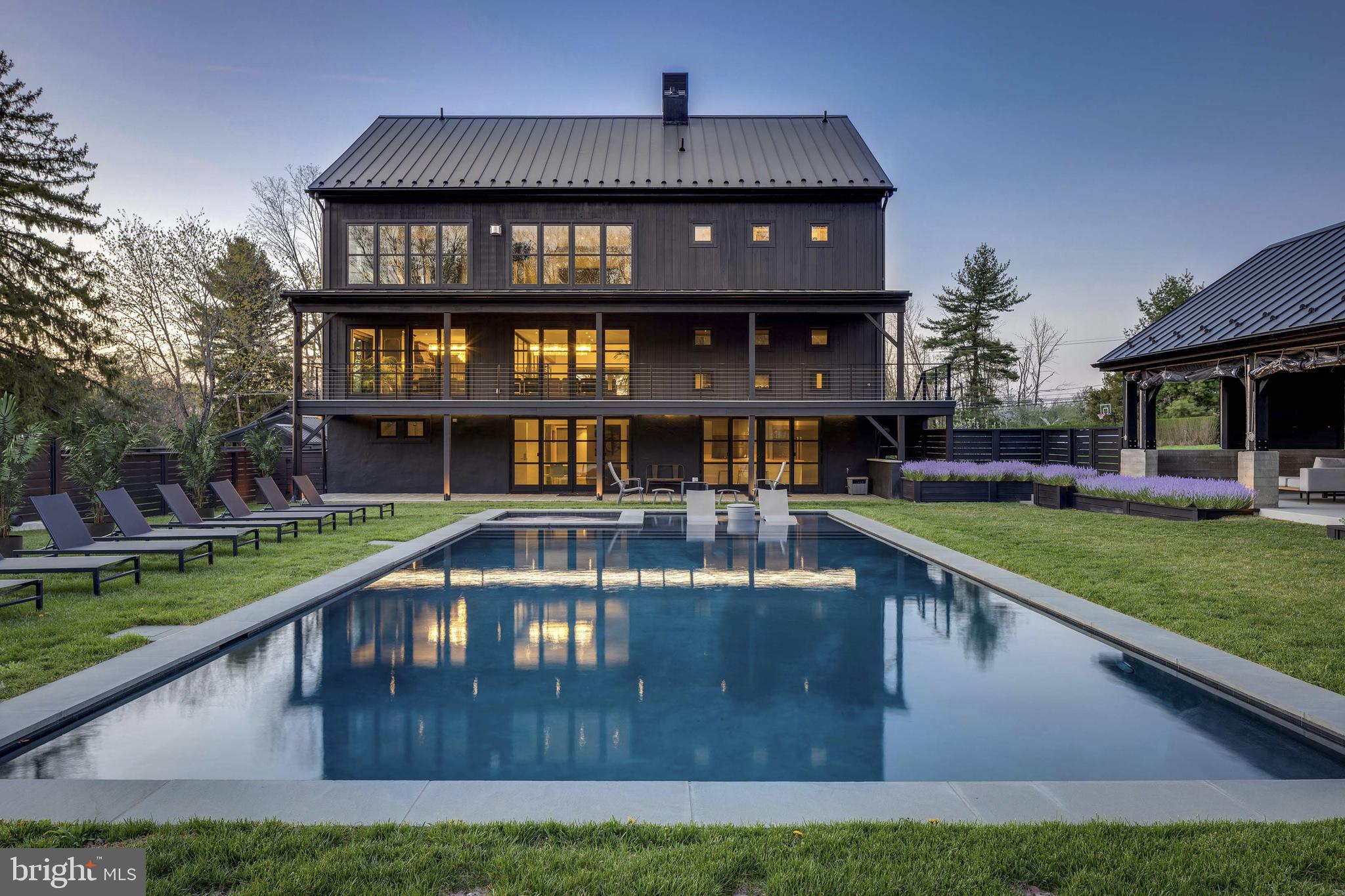Welcome to a truly exceptional property where innovation, luxury, and sophistication come together. This magnificent estate, spanning over 10,000 square feet and nestled on a sprawling 10.5 acre lot, is a one of a kind home that offers both unparalleled comfort and cutting-edge design. Located in the heart of Bucks County, this residence blends modern living with forward-thinking technology, making it a standout in New Hope’s real estate landscape. Designed with purpose and built for luxury, the home spans four living levels serviced by an elevator and a stunning floating steel stair tower enclosed in glass. The expansive main living area is highlighted by an impressive bar featuring illuminated glass shelving set against smoked mirrors, flanked by two 450-bottle wine cellars, perfect for wine lovers and entertaining guests. The chef’s kitchen is a culinary masterpiece, complete with a custom-built La Canche range from Paris, Sub-Zero fridge and freezer, and Miele appliances offering versatility and precision. The cabinetry was designed specifically for the space by Plato, and the expansive island comfortably seats eight, making it a perfect spot for gatherings. With six spacious bedrooms, each featuring its own en-suite bathroom and custom closets, this home ensures both privacy and comfort for all. The top floor offers a tiered movie theater with a bar and gaming center, ideal for cinematic experiences and entertainment. The bottom floor features an additional chef’s kitchen, perfect for hosting gatherings. Outside, you’ll find a luxurious heated pool and spa, surrounded by imported palm trees, a Sonos sound system, and an outdoor shower for added convenience. In addition to the main residence, the property boasts three impressive outbuildings. The first is a remarkable 1,300-square-foot event PAVILION, heated with seasonal enclosures and furnished with contemporary pieces that create an elegant atmosphere. Inside, you’ll find a 22-seat bar with three TVs, a hanging fireplace imported from France, and a fully stocked outdoor chef’s kitchen. This kitchen includes a pizza oven, Japanese Hibachi tables, and a custom-built smoker making it a dream for grilling enthusiasts. Adjacent to the home is a Hampton-inspired guest cottage, featuring a bedroom and full bathroom providing a private retreat for guests. The property also includes a spacious 1,500-square-foot bi-level CARRIAGE HOUSE, complete with a bedroom, full bathroom, state-of-the-art fitness center, dance studio, and an upstairs office with a full kitchen and bathroom that can be converted into a separate residence. These exceptional amenities provide the ultimate setting for relaxation, entertainment, and an elevated lifestyle.