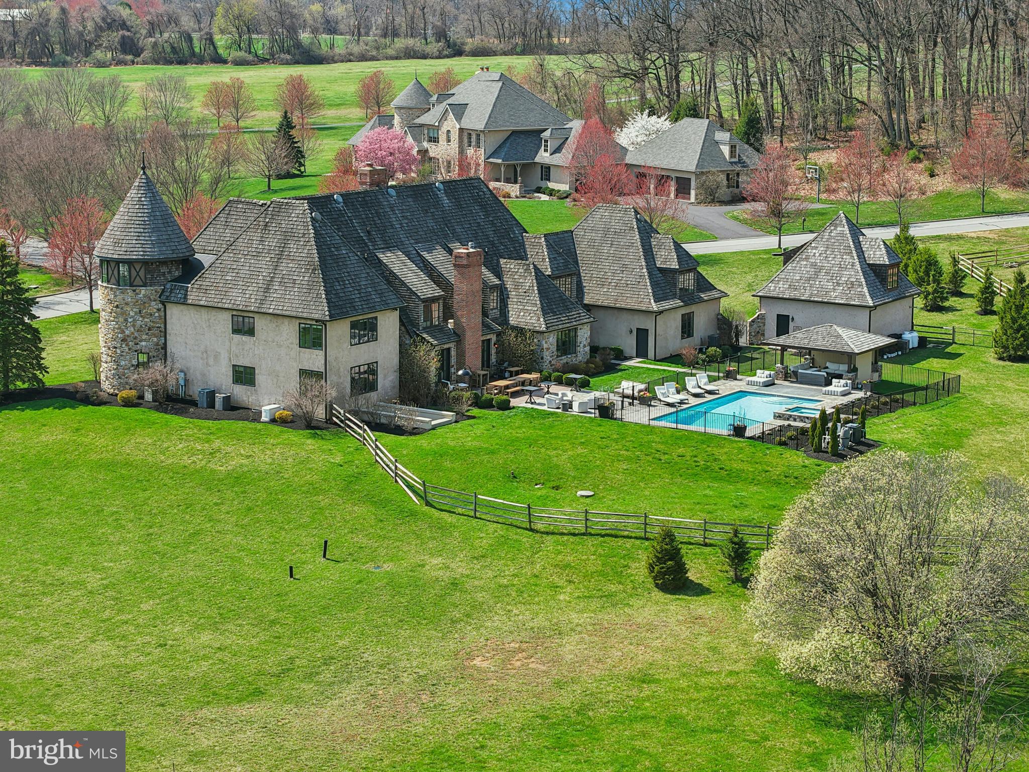 This magnificent home is evocative of the graceful splendor of old houses one might find nestled deep in the French countryside. Built by Myron Haydt for his personal residence in 2011, this 8,800 square foot home has an architectural style and interior design that is at once timeless and innovative. European influences are evident in the stunning fieldstone and brick exterior, dramatic cedar shake rooflines, and captivating turrets. Paver walkways and a welcoming drive lead to 5 car garaging as the first approach to this prestigious home, centered on 2.5 acres.
Inside, the home embodies a gentle blend of grace and subdued elegance. Rooms are bathed in light through oversized Pella windows and French doors. Ceilings are ten feet high on the main and lower levels and nine feet on the second. The many luxurious amenities include thick oak and marble floors, extra high baseboards, deep crown moldings and curved walls. There is a stunning kitchen, combining beauty and functionality, with a custom wood coffered ceiling, solid marble countertops, and stainless appliances. The adjacent breakfast nook has a vaulted ceiling and three walls of windows to let in natural light in every season. Nearby, the cozy family room has a wood-burning fireplace with marble surround, and two sets of French doors opening to the back yard. 
Spacious primary bedroom suites are found on both the main and second levels, welcoming use by extended families. These suites boast large windows and sumptuous baths appointed with marble floors, jetted tubs, walk-in showers, and custom vanities. The second floor primary suite boasts extraordinary size and comfort, with a gas lit fireplace and a curved stairway that takes you to a lofted room overlooking valley views and beckoning one to enjoy a private getaway or office retreat. Three additional ensuite bedrooms and a second floor laundry room offer the amenities that one would expect from a home of this caliber.
A newly updated lower level includes a bar, theatre room, gym, family room and wet bar,  as well as a full bath with steam shower. The attached 3-car garage is complemented by a heated 2-car detached garage with loft space, ready to be customized. The heated pool and spa, new pool house, and intricate paver patios are accessed from the sunroom and family room for intimate dinners under the stars or lively celebrations.
Melrose Manor is a modern estate with old-world charm, in a distinguished Saucon Valley neighborhood where shopping, dining, and entertainment venues are just minutes away.