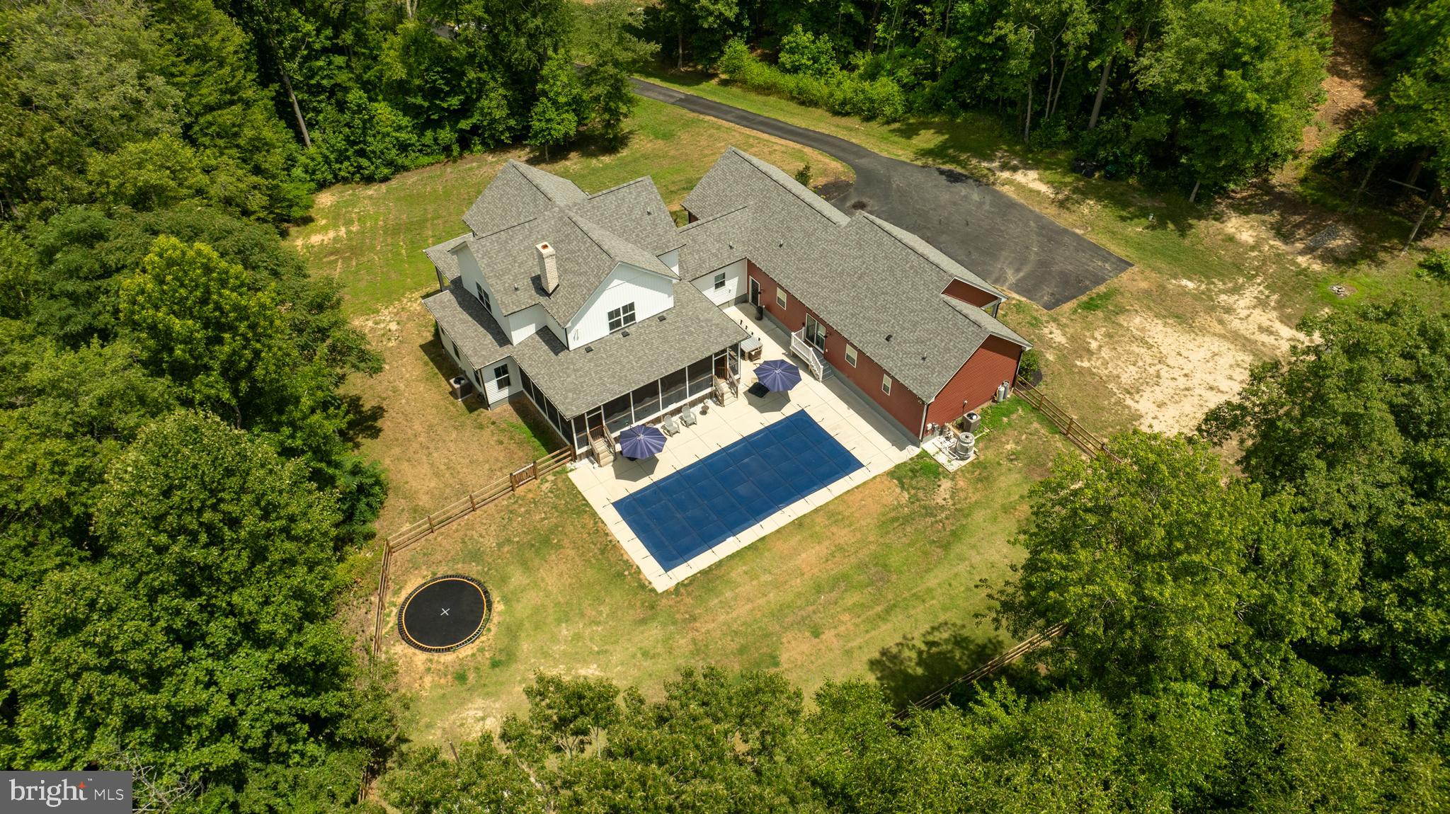 Discover unparalleled privacy and tranquility in this custom-built home, privately nestled within a lush pocket of trees off a secluded cul-de-sac. Situated on 3.6 acres of serene woodland, this residence offers the perfect escape from the hustle and bustle of everyday life. As you approach the main home, you're greeted by an expansive front porch with elegant brick trim—ideal for enjoying a morning coffee while immersed in nature. Enter through the garage into a well-designed mudroom featuring a built-in arrival center, designed to keep your daily essentials organized. Adjacent is a large laundry room for added convenience. The open-concept living area is the heart of the home, highlighted by beautiful wooden pillars that add a touch of rustic elegance. The kitchen is a chef's dream, complete with a large island featuring a farmhouse sink, a custom-built wood range hood, and a secure walk-in pantry complete with its own access code. The inviting family room centers around a brick wood-burning fireplace flanked by custom built-ins, creating a warm and welcoming atmosphere. Down the hall, the primary bedroom is a private sanctuary with its own access to the screened-in back porch, a spacious walk-in closet, and a luxurious ensuite bathroom with a soaking tub, TV, and dual vanities. Additional features on the main level include a built-in desk under the stairs and a cozy reading nook / work area. Ascending the integrated illuminated hardwood stairs, you'll find a second-story family room with walk-in closet storage. This level also houses two large bedrooms that share a Jack & Jill bathroom and a spacious third bedroom with its own ensuite bathroom. The expansive screened-in porch, accessible from the family room through two sets of French doors, overlooks a fenced-in backyard oasis. Perfect for entertaining, this outdoor haven includes a TV, a saltwater pool with a pool chiller, an inground trampoline, and a firepit plus 2 year old fence. The attached in-law suite is a perfect blend of comfort and style, featuring a spacious front porch for relaxing. Inside, the family room is outfitted with built-ins that are roughed in and ready for a gas fireplace. The open-concept continues with a kitchen and dining area ideal for modern living. The primary bedroom offers a walk-in closet and an ensuite bathroom with a soaking tub. This in-law suite also includes a bonus room for use as an office or den, its own laundry room, and direct access to the shared garage and backyard oasis. This stunning property is conveniently located just 15 minutes from Fairview Beach to the east and downtown Fredericksburg to the west, offering both peaceful seclusion and easy access to amenities. Experience the perfect blend of luxury, privacy, and natural beauty in this exceptional home, your personal sanctuary amidst the trees.  Major income potential.