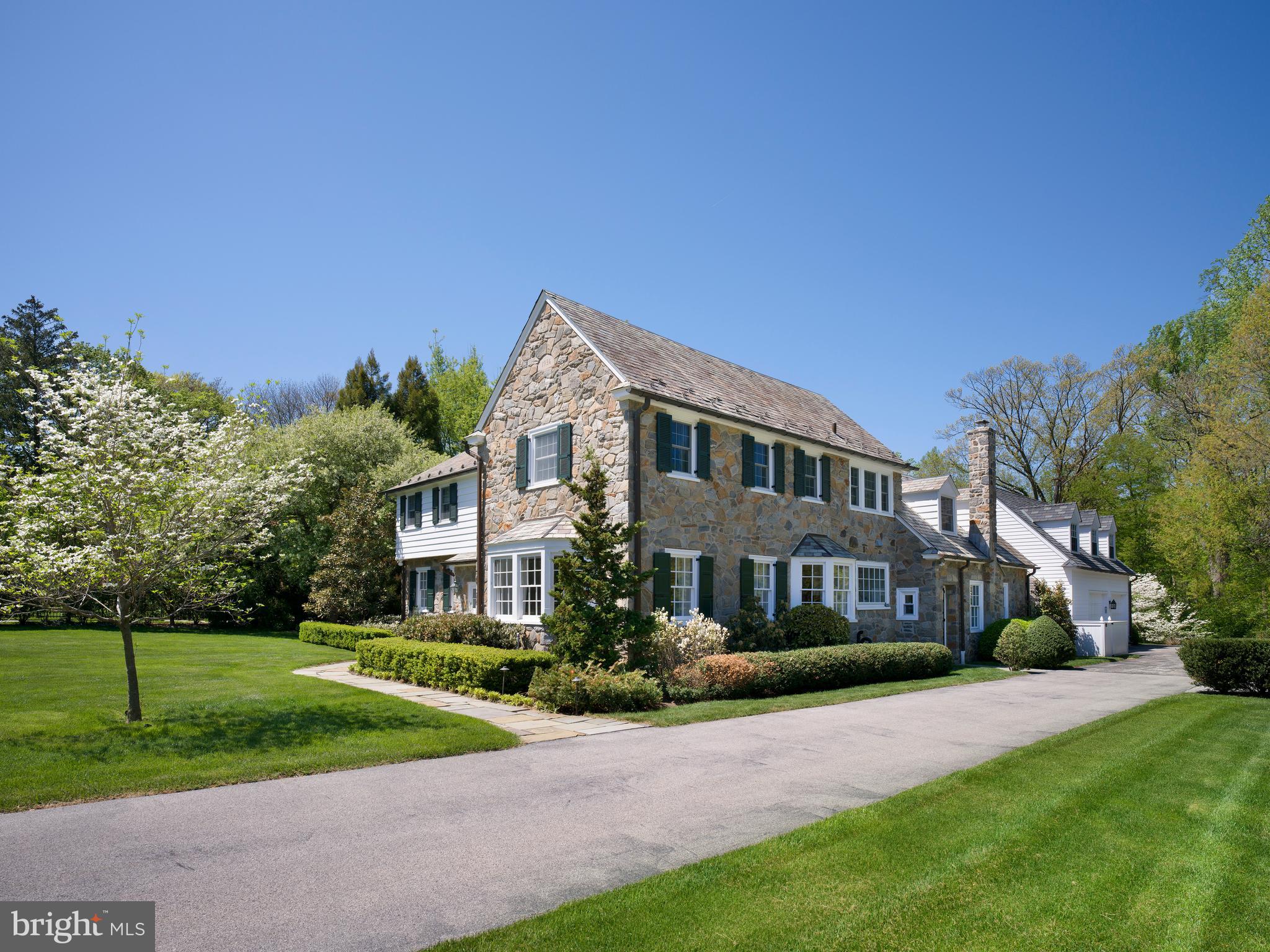 Weekend open houses are cancelled on Sat April 25 and Sun April 26. Set at the end of a Wynnewood cul-de-sac, surrounded by homes of similar scale and character, this stone Colonial draws equal strength from its setting and its architecture—expanded through an executed addition by EB Mahoney Builders that preserves the proportions and craftsmanship of the original home while delivering the space and flow expected today.

A vestibule entry opens to a traditional center-hall plan with hardwood floors throughout. The wood-paneled library, anchored by a fireplace and served by its own powder room, connects to a sunroom wrapped in stone and beadboard—a light-filled space that also opens to the living room and kitchen, establishing a natural flow across the main level. The living room, with a second fireplace and windows on multiple exposures, sits opposite a formal dining room, where a deep bay window frames views of the front grounds and mature specimen trees.

At the center of the home, the kitchen—reworked as part of a later renovation—is anchored by an expansive center island with seating, complemented by full-height custom cabinetry and a bright breakfast area. The space opens directly to the sunroom and adjoining family room, reinforcing the flow of the main level and supporting both everyday use and entertaining. A mudroom, second powder room, and access to the oversized garage complete this level.

Upstairs, a central landing leads to a private primary suite with a walk-in closet and double-vanity bath. Four additional bedrooms and three baths complete the second floor with a well-balanced layout.

The lower level is filled with natural light from oversized window wells and features a stone fireplace along with custom built-in desk workspaces, creating a flexible area for work, study, and everyday use. Storage and mechanical spaces are substantial and well organized.

A flagstone terrace overlooks broad, level rear grounds—uncommonly usable space suited for sports, play, and larger-scale outdoor living. The home has been extensively improved and consistently maintained over time, with a comprehensive addition, subsequent renovations, and significant landscaping and hardscaping enhancements.

Ideally located in Lower Merion Township, with convenient access to Suburban Square, regional rail, and Center City.