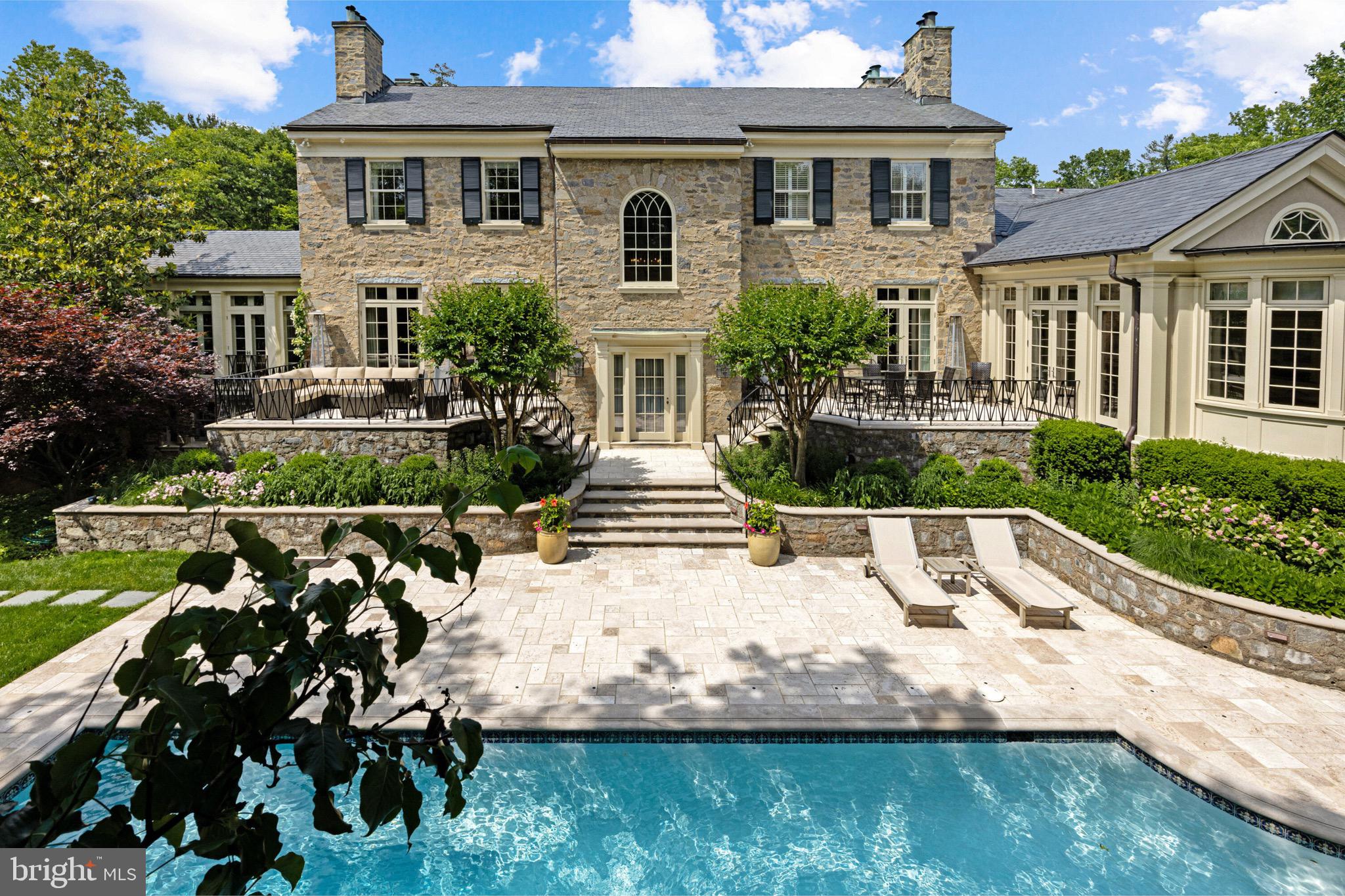 One of the finest architectural wonders of the Capital Region, 2 Oxford Street is a legendary address prominently sited in the heart of Chevy Chase Village, just over the District line. Originally conceived in 1918 by renowned Washingtonian architect Waddy Wood, designer of the Chevy Chase Club and countless storied buildings in the city, the estate has undergone a meticulous transformation headed by an acclaimed partnership between architect David Jones and master builder Richard Zantzinger. The result is a masterpiece of painstaking preservation married to modern functionality within an estate of unparalleled workmanship and attention to detail. Upon approach, the estate’s fieldstone exterior and verdant landscaping evoke images of centuries-old manor homes in the upper northwest. Nestled beneath elegant contrasting trim is the original entry door, opening into a grand reception foyer accented with original moldings and inlaid crosscut limestone floors. Throughout the home, original details faithfully preserved in their original grandeur blend with bespoke custom finishes within a floor plan equal parts formal and livable. Polished nickel hardware by Enrico Cassina imported from Italy adds a touch of bygone craftsmanship. Formal living areas comprise one wing of the main level, introduced by an old-world den with a custom bar, original knotty pine walls and molding, and an original woodburning fireplace, one of seven in the home. An ethereal library with French exterior doors and a generously proportioned living room with original floors and a roaring fireplace complement the space. Opposite the foyer, the formal dining room’s coffered ceiling, honey onyx marble chair rail, and hand-cut inlaid Rossa Verona flooring impart a warm ambiance. Constructed brand new as an addition in 2011, the elegant Downsview kitchen is a modicum for luxurious functionality. Stunning tilework includes the custom backsplash matching Azul Bahia granite countertops and Jerusalem crosscut travertine flooring laid out in a Versailles pattern. Furniture grade cabinets conceal redundant Viking, Miele, and SubZero appliances. The primary suite is opulently appointed with its original fireplace, motorized blackout blinds, and twin dressing rooms with built-ins. The lavish ensuite bath is clad in white marble with honey onyx accents and features a walk-in steam shower with an instant hot water system as well as a jetted tub. Four secondary bedrooms, two ensuite and two Jack-and-Jill, feature custom tiled baths. A large laundry room and storage space completes the upper level. The lower level sits above ground and is thus flooded with natural light. Its showstopper is a custom 2,000 bottle, temperature-controlled wine vault with hand painted ceiling by local artist Lenore Winters. A synthetic ice rink with perimeter boards, windowed fitness room, and nanny suite complete the space. The estate’s stunning grounds are an artful blend of hardscaping and verdant foliage. Travertine terraces spanning the width of the home are accessed via French doors to establish an indoor/outdoor relationship, while the 50-foot replastered saltwater lap pool shimmers under fountain jets. The standalone pool house has a collapsible Nanowall and is equipped with its own HVAC system and full kitchen. A built-in grill, fire pit, and custom planters designed by David Jones complement the whimsical outdoor spaces.  Multi-zoned geothermal HVAC, full audio/visual capability, comprehensive security, full waterproofing, and commercial-grade insulation, slate roofing, copper gutters, and structural reinforcements make the home a fortress. Embodying the very ethos of Chevy Chase Village and representing its illustrious history, 2 Oxford Street also introduces a meticulous attention to detail to create not only a splendid blend of old and new, but one of the Capital Region’s timeless estates.