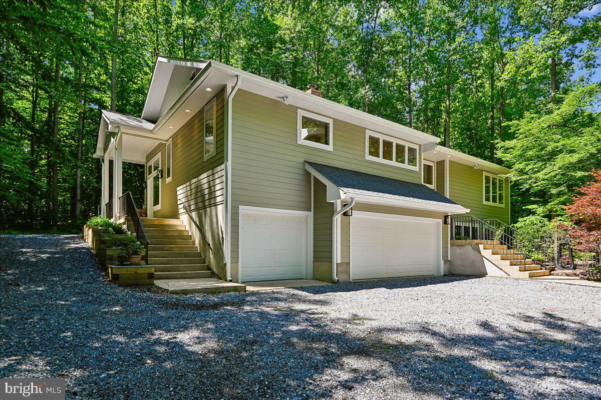 A private Davidsonville retreat offering the perfect balance of privacy and accessibility, this custom-built, privately sited contemporary 4 bedroom, 3 ½ bath home with rarely available 3-car garage is nestled on 2.32 acres of mature trees, landscaped gardens, and natural beauty while also being located within the Davidsonville school district. Designed for everyday living and effortless entertaining, this exceptional property combines peaceful rural serenity with everyday convenience—and must be experienced in person to be fully appreciated. Showcasing distinctive architectural details and quality craftsmanship throughout, the home features hardwood and tile flooring, vaulted ceilings throughout main level, interior soffits with up and downlighting, low maintenance composite multi-level deck, James Hardie siding and architectural shingle roof (both new in 2025), an abundance of casement windows—smartly located under 3-foot eaves, two large roof window for added natural lighting, and over 100 light fixtures, including recessed, pendant lighting, and additional custom lighting. The open-concept main level is anchored by a dramatic wall of glass that brings the outdoors in, complemented by a handcrafted masonry fireplace with heated bench and pizza oven. Extending the great room, the chef-style kitchen and dining area offer seamless flow and function, featuring abundant custom Brookhaven dual-tone cabinetry, a spacious walk-in pantry, Frigidaire professional refrigerator and freezer units, Thermador range hood with heat lamps, and a large island with prep sink, and butcher block counter for baker’s workspace. The dining area includes built-in display cabinetry, making it ideal for both casual meals and hosting gatherings. The primary suite is a true retreat with wooded views, a sitting room, vaulted ceilings, a large walk-in closet, and a spacious bath with deep soaking tub, separate shower, and double sink vanity. A large guest bedroom with lovely views, hall bath with tile flooring, laundry room with upgraded front loading Electrolux washer and dryer as well as extensive shelving, and powder room with decorator storage ledge complete the main level. The lower level is equally well-appointed with a recreation room featuring a tray ceiling, wet bar, pantry, refrigerator, and travertine tile flooring, two additional bedrooms (one currently used as a home gym) with full daylight windows overlooking the front gardens, a full bath with new vanity and quartz countertop (2026), and direct access to the spacious garage, workshop room with industrial vinyl flooring, and additional utility/storage room. Additional recent (2025/2026) improvements include 6" gutters, fresh interior paint, and new carpet in the lower-level bedroom. The outdoor setting invites you to explore and enjoy the sounds and views of nature, lovely garden beds, raised garden boxes, and wooded surroundings. Nearby Davidsonville Park (approx. 2.5 miles) offers trails, athletic fields, playground, cartop boat launch, fishing, and pavilion rentals. Convenient access to commuter lots (less than 6 miles), popular cycling routes, MD Routes 424 and 214, and easy connections to US-50 provide straightforward commuting to Annapolis, Washington, D.C., and BWI Airport. Don’t miss this exceptional opportunity to make this special property your own.