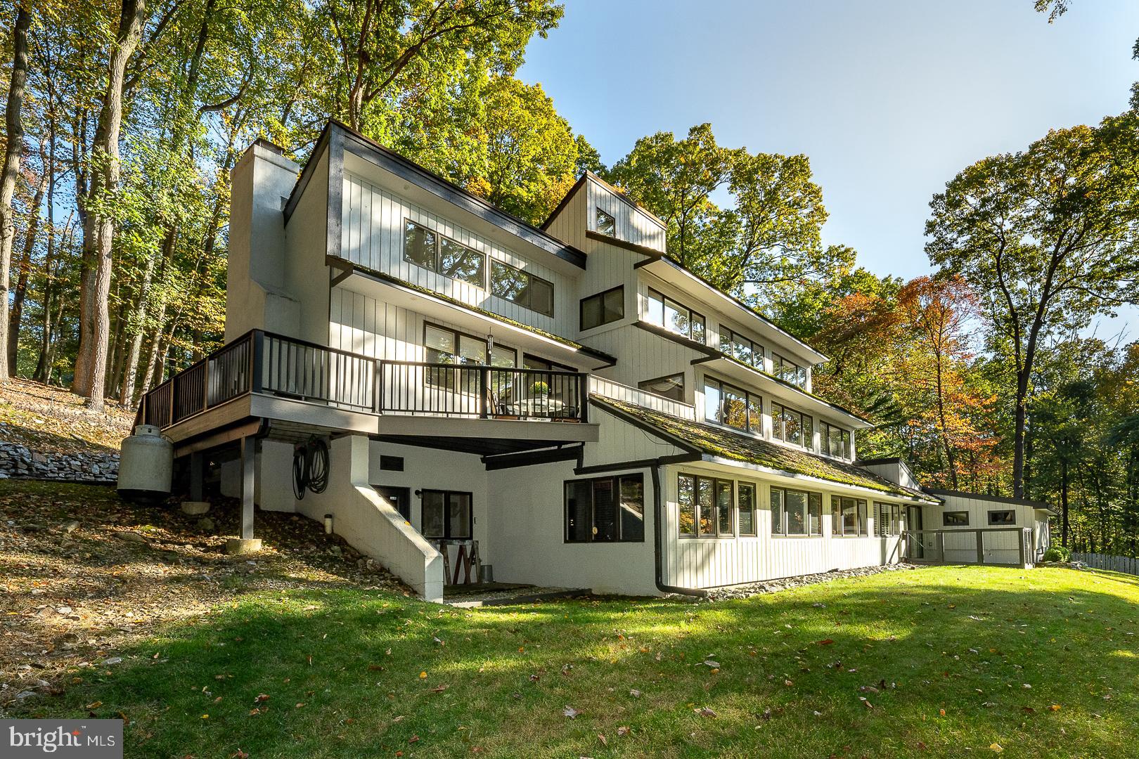 Tranquility awaits you at this one of a kind three level contemporary sitting on 2.5 wooden acres on desirable Rochambeau Drive on Valley Forge Mountain. This location provides a blend of nature and serenity and is being offered for the first time in 40  years.  It is in the acclaimed Tredyffrin Easttown school district. The views from  all the windows  facing Rochambeau Drive are spectacular. The  Main entrance hosts a wide entrance hall with hardwood floors leading to an oversized dining room with hardwood floors, wainscotting and a crystal chandelier. One step up frm the foyer is a cathedral ceiling living room with hardwood floors, a beautiful stone gas fireplace and a slider to a Trex deck.  An alcove  around the corner from the entance is the coat closet plus a powder room.  The  white kitchen has been updated , has granite tops, new lighting and floors, plus a breakfast area with  a desk area and cabinets.  The views from the kitchen sink are fabulous!  Adjacent to the breakfast area is a bright sunroom with skylights, a ceiling fan  and an egress to the large Trex deck. Upstairs is the primary bedroom suite.  It is carpeted and has a large walk in closet plus 2 other closets  and  a pocket door to a very spacious updated bath with a  shower, 2 sinks, a bench, make up area with mirror, marble floors and a jacuzzi.  At the other side  of the main bath is a dressing area with 2 closets, hardwood floors  and a ladder  to a loft.  From the loft you can enter the attic which is floored and has an attic fan.
The lower level has 3 or 4 bedrooms and 2 baths.  The largest of these rooms could be an in-law  or aupair suite or a family room.  It has a pocket door to a small entrance and an exit to the outside plus acess to the attached 2 car garage.  This room has an attached bath,  cedar lined closets , 2 skylights, ceiling fan, recessed lights, plantation shutters, a built in desk area and a slider to an ouside garden area.  There are 3 other bedrooms  with a hall bath.  The largest of these 3 bedrooms is currently used as an office.  It has built in bookcases  and could possibly be a playroom.  On this level there is a laundry with a sink and many cabinets,  plus a workshop with an outside exit,  a furnace room holding the less than a year old  furnace, a linen closet and a hallway wet bar. There is an attached 2 car garage  which holds the 2 new oil tanks in it's rear plus a storage area above. There is also a carport and you will notice parking for many cars.  On the right side of a special parking ares is a one year old shed.