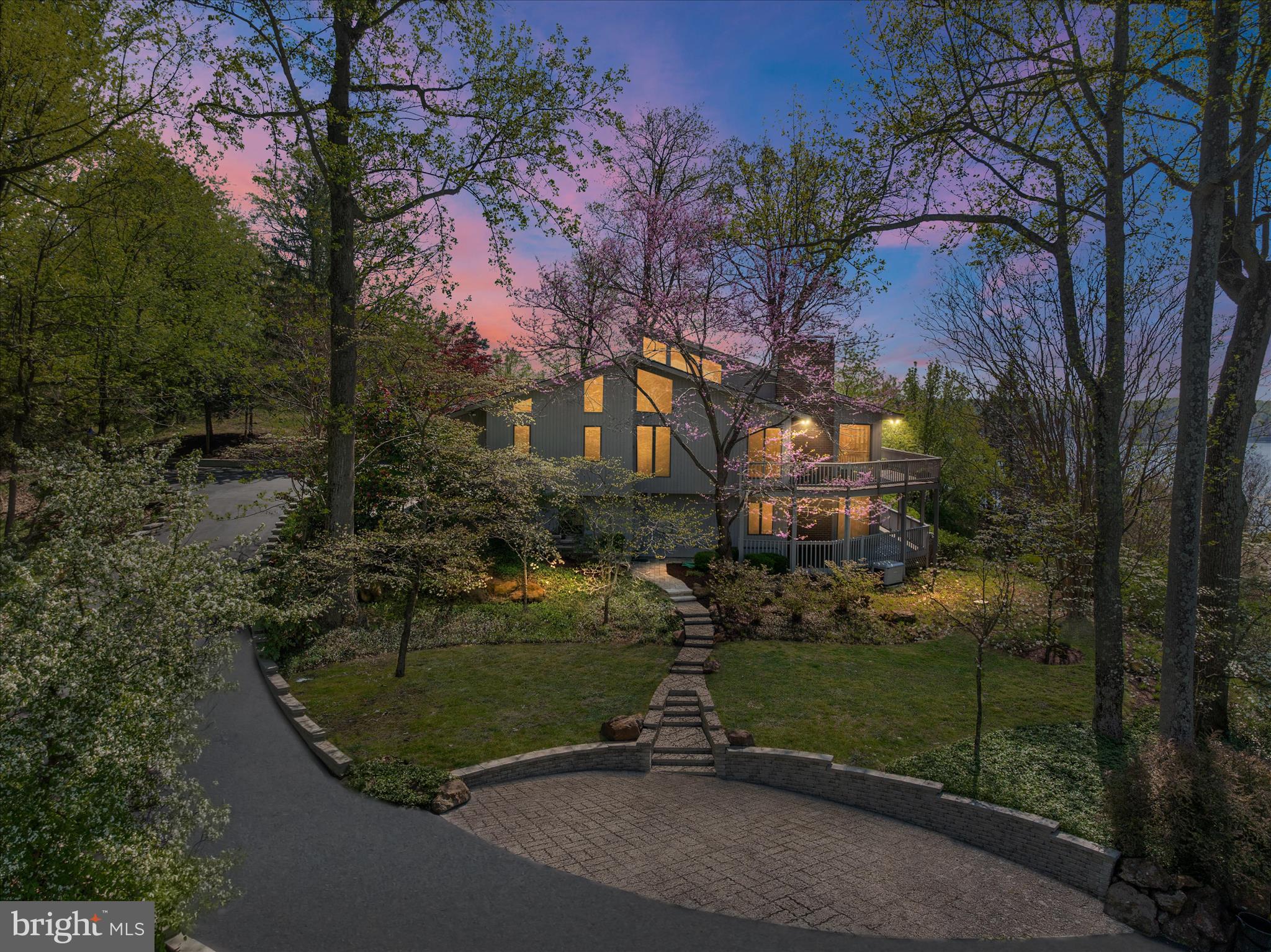 Set along one of the most coveted stretches of the Severn River, this extraordinary residence in Rugby Hall Estates offers a rare blend of architectural distinction, sweeping water views, and seamless access to the region’s most desirable destinations, all enhanced by the unique opportunity to enjoy front-row views of the Blue Angels air show right from your own waterfront setting this year. Nestled on 1.27 acres of serene, tree-framed landscape, the home captures commanding views of the widest part of the Severn, a breathtaking panorama that becomes the backdrop to daily life. Inspired by Californian architecture, the design embraces light, volume, and effortless indoor and outdoor living. Expansive glass and an open floor plan create a natural flow between the generous kitchen, dining area, and great room, all oriented to maximize the river views. Just off the main living space, a stunning four seasons room provides a light-filled retreat where walls of windows frame the water, offering year-round enjoyment of the landscape in total comfort.
A dramatic two-story deck extends the living space outdoors, offering the perfect setting for sunset entertaining or quiet mornings overlooking the water. While there is not currently a pool on the property, thoughtfully prepared plans have been provided to help you envision a future private pool oasis, allowing the next owner to create a custom outdoor retreat tailored to their lifestyle. The expansive, private setting offers the ideal canvas should you choose to pursue it. The thoughtfully designed mudroom addition provides elegant functionality, seamlessly connecting the two-car garage to the main living spaces.
The main-level primary suite is a private retreat, where tranquil river views greet you each morning. Upstairs, a charming third-floor loft offers flexibility for a refined home office, creative studio, or secluded reading lounge. The fully finished lower level features three additional bedrooms, two full baths, and an oversized great room anchored by a stunning fireplace, all complemented by remarkable water views that continue throughout the home. A long, private driveway enhances the sense of exclusivity and arrival. Beyond your personal sanctuary, Rugby Hall Estates offers an exceptional waterfront lifestyle with private community access to the Severn River, including a pier with slips and moorings, boat ramp, kayak and paddleboard storage, pavilion with an upcoming renovation in the fall, playground, and scenic walking paths connecting directly to the B and A Trail. Located within the highly regarded Severna Park school district and offering immediate access to major commuter routes, including Route 50, 97, 695, and 95, this home provides effortless connectivity to Baltimore, Washington, D.C., and beyond, while preserving the privacy and tranquility discerning buyers expect. This is more than a home. It is a rare opportunity to own a legacy property in one of Maryland’s most prestigious and tightly held waterfront communities.