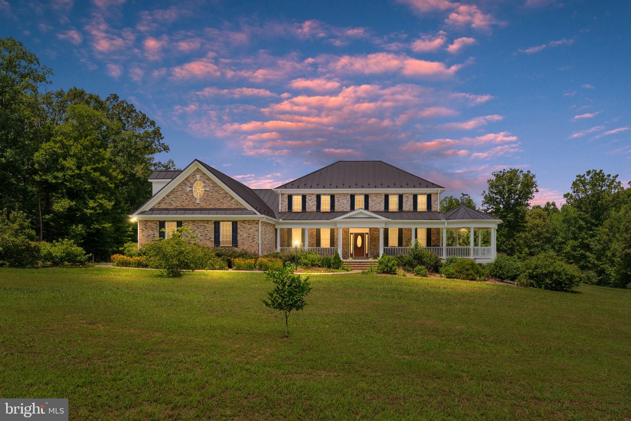 Welcome to a place where timeless craftsmanship meets the freedom of country living. Nestled in the heart of 86 breathtaking acres of mature hardwoods, this exceptional custom-built farmhouse is perfectly positioned in a sprawling clearing, creating a private estate unlike any other. Approximately 15 acres are cleared, offering the perfect setting for horses, farming, livestock, gardens, or simply enjoying wide-open spaces, while the remaining hardwood forest provides complete privacy, abundant wildlife, and endless recreation.

The property itself is a destination. Private trails wind throughout the hardwoods, inviting horseback riding, hiking, ATV adventures, hunting, and peaceful walks beneath the towering trees. A picturesque stream meanders through the property, adding natural beauty and the soothing sounds of flowing water. With the ability to subdivide and a separate road entrance already in place, this estate offers outstanding long-term investment potential while preserving the privacy of the main residence.

Built with a level of craftsmanship rarely found today, the home showcases all-brick construction, solid wood doors, 6-inch exterior walls for superior strength and energy efficiency, and a true raised-seam metal roof with snow guards, ensuring lasting beauty and durability. A welcoming deep wraparound porch invites you to slow down, relax, and enjoy panoramic views of the surrounding countryside.

Inside, timeless finishes include rich cherry cabinetry, custom built-in bookcases, oak flooring, ceramic tile, beadboard ceilings, elegant wainscoting, and classic glass doorknobs. The thoughtfully designed floor plan features two spacious primary suites—one on the main level and one upstairs—plus two additional bedrooms, three full baths, and a half bath, making it ideal for multi-generational living or hosting family and friends.

The chef's kitchen offers cherry cabinetry, an LP gas cooktop with exhaust hood, double wall ovens including a convection oven, trash compactor, central vacuum sweep inlet, and abundant workspace. The adjoining family room is anchored by a cozy LP gas fireplace with blower and remote.

Designed for year-round comfort, the home features three heat pump systems, an electronic air filtration and humidification system, an insulated conditioned crawlspace, a homeowner-owned 500-gallon buried propane tank, deep 500-foot well, gravity-fed septic system, Firefly fiber-optic high-speed internet, and a cell phone signal repeater.

Outdoor amenities continue with an 18-foot above-ground pool surrounded by composite decking, a 48' x 31' metal barn with 100-amp electrical service ideal for horses, equipment, or a workshop, a workshop-ready garage with generator transfer switch, walk-in attic storage, magnetic driveway alarm, and a private half-mile gated driveway leading to your secluded retreat.

Whether your dream is a premier horse farm, working farm, recreational paradise, or legacy family estate, this extraordinary property offers an unmatched combination of luxury construction, exceptional privacy, natural beauty, and future investment potential that is rarely available.