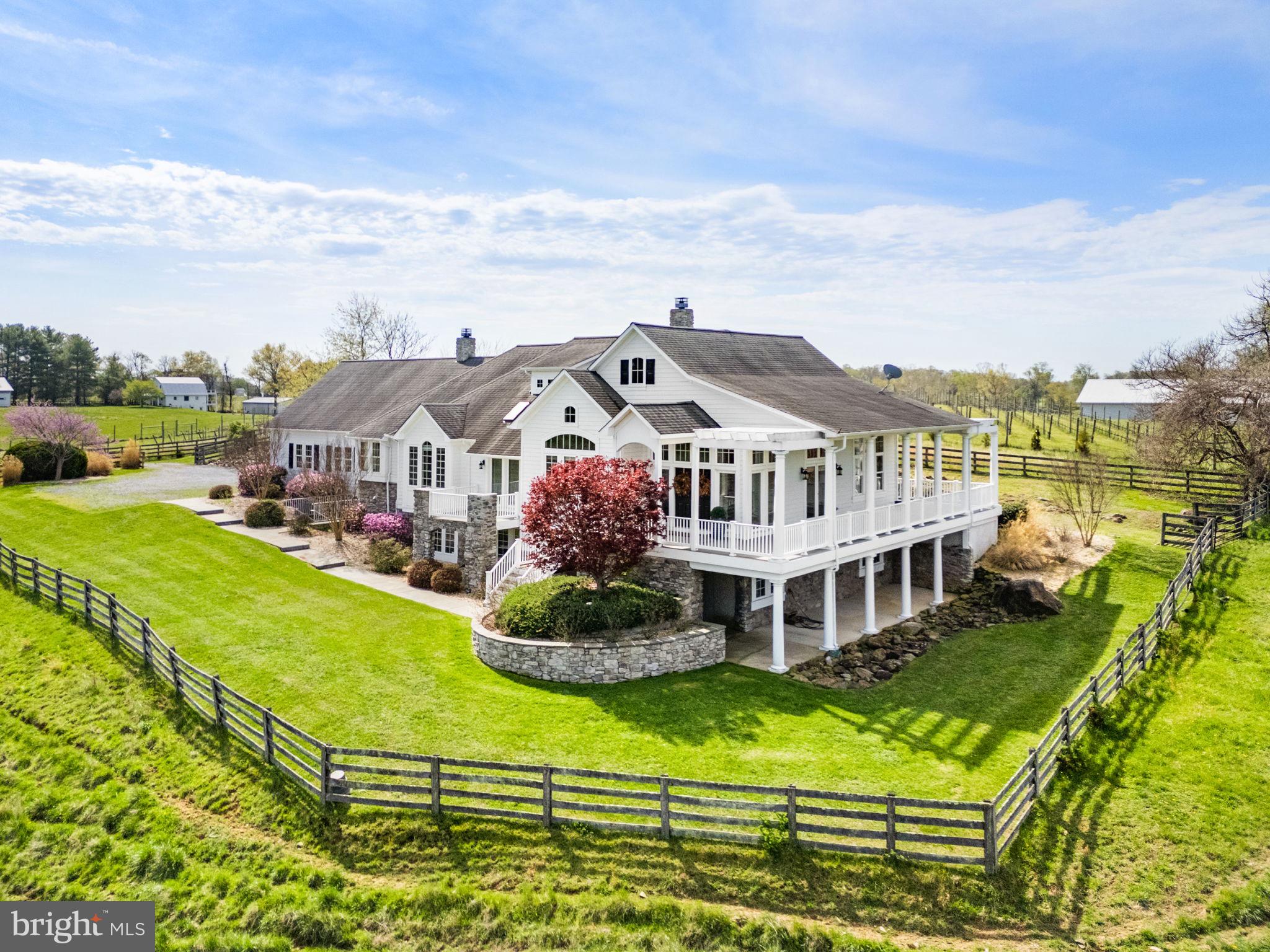 Nestled on over 14 private acres across 2 parcels, this exceptional custom Chadsworth estate offers refined country living just minutes from Round Hill and western Loudoun amenities. This property blends timeless craftsmanship, expansive living spaces, and breathtaking natural surroundings in a premier rural setting with no HOA.

A stately stone and HardiPlank exterior welcomes you to a thoughtfully designed residence featuring nearly 5,700 finished square feet across two levels, with additional unfinished space reflected in tax records. The main level offers true one-level living, anchored by a luxurious primary suite with hardwood floors, tray ceiling, spa-inspired bath with jetted tub, walk-in shower, his and her reading lights and generous walk-in closet (one of eleven total closets within the property). Additional main-level spaces include a formal foyer, sitting room, private office with two sets of French doors, den with built-ins, formal dining room with skylights and balcony access, and a warm living room with double-sided electric fireplace.

The country-style kitchen is both functional and inviting, featuring granite countertops, center island, double wall ovens, ENERGY STAR stainless appliances, skylights, and abundant cabinetry. The adjoining breakfast room includes a second electric fireplace and views of the surrounding landscape. A large mudroom and main-level laundry add everyday convenience.

The fully finished walkout lower level offers remarkable flexibility with four additional bedrooms, multiple Jack-and-Jill baths, a recreation room, bonus room, and den—ideal for guests, multi-generational living, or home-based workspaces. Each bedroom offers generous proportions, walk-in closets, and access to full baths.

Architectural details throughout include vaulted, tray, and two-story ceilings, hardwood flooring, chair rail and wainscoting, recessed lighting, skylights, and expansive windows that frame pastoral and creek views. The home is equipped with zoned HVAC, propane-owned heating system, humidifier, dehumidifier, air filtration system, and energy-efficient windows and appliances.

Outdoors, the property offers endless possibilities—gardening, recreation, or simply enjoying the serenity of creekside living. The attached side-entry two-car garage complements the home’s thoughtful layout, while the rural AR-1 zoning provides flexibility and multiple of potential use options.  The 30'x50' metal barn/workshop with electric coupled with the two stall run-in at the back of the property offer significant possibilities for future use. 

Conveniently located near Route 7, historic Round Hill, wineries, and outdoor recreation, and served by Round Hill Elementary, Harmony Middle, and Woodgrove High School, this rare offering combines acreage, water frontage, and luxury living in one of Loudoun County’s most scenic settings.

Note: aerial photography property lines on photos are an approximate estimation.