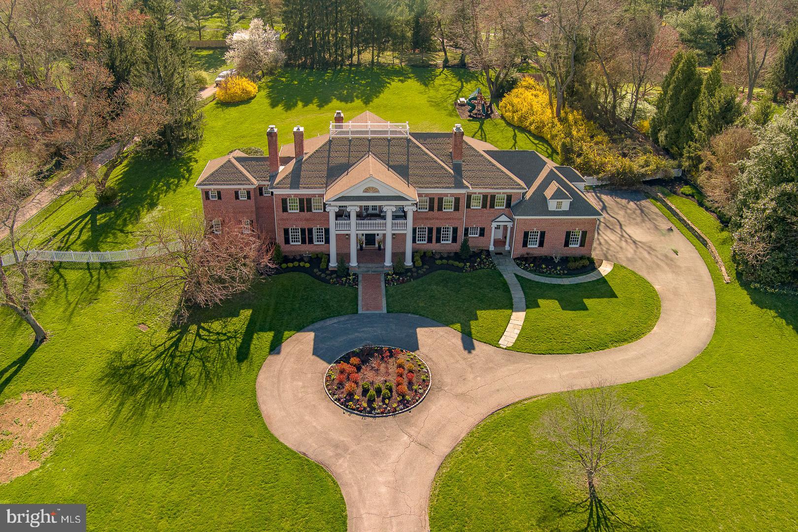 Step into the grand foyer of this Georgian-style home and be greeted by the warm embrace of traditional elegance seamlessly blended with modern luxury. Recently featured in Traditional Home Magazine alongside renowned interior designer Glenna Stone, this nearly 9,000-square-foot estate overlooks Philadelphia Country Club in the coveted Gladwyne neighborhood, a true suburban oasis.
As you enter through the arched doorway, the great room beckons with its 28-foot-high wood trusses and beams, infusing the space with a sense of comfort and sophistication. Expansive windows and French doors invite the outdoors in, offering breathtaking views of the surrounding landscape.

A graceful curved staircase leads to a circular landing and balcony on the upper level, creating an ideal setting for entertaining against the backdrop of the picturesque golf course. The dining room, adorned with a painterly emerald green silk wall covering and a cozy fireplace, exudes an elevated charm perfect for intimate gatherings. Tucked behind pocket doors, the living room strikes a balance between formality and comfort, boasting exquisite molding, built-in bookshelves, and a marble fireplace.The fully remodeled kitchen is a vision of contemporary elegance, featuring Giotto quartzite countertops, an oversized island, and slate blue cabinetry bathed in natural light. This level also offers a spacious powder room with unique tile flooring and brass accents, while a sun-soaked home gym and a vibrant, multifunctional office space cater to wellness and productivity.

The primary suite is a haven of luxury, complete with a cozy sitting area, a pass-through coffee bar, featuring a mini refrigerator and compact dishwasher that is perfect for enjoying a morning cup of coffee or a relaxing evening beverage without leaving the comfort of the suite. Indulge in a spa-like bathroom with heated tile flooring and a freestanding bathtub. Upstairs, two generously sized bedrooms each boast a fireplace and walk-in closet, sharing a large bathroom. A fourth bedroom features a beautiful bay window overlooking the expansive rear property, complemented by an en suite bathroom and walk-in closet. The fifth bedroom offers a private suite with its own ensuite bathroom, providing a serene retreat for guests or family members.

This exceptional home seamlessly marries traditional charm with modern comforts, creating an unparalleled living experience in one of Gladwyne’s most prestigious locations. Welcome to a timeless sanctuary where luxury and sophistication converge.
