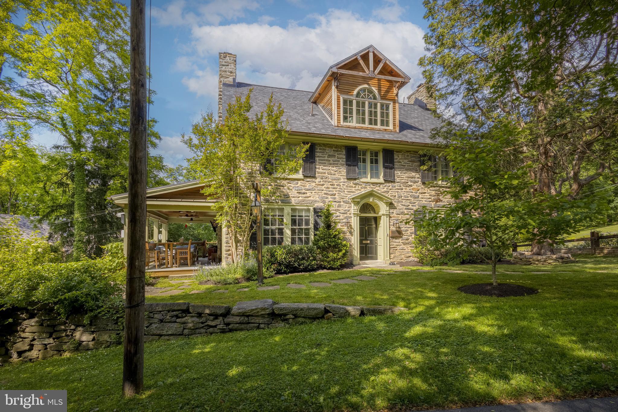 Welcome to this beautifully reimagined Chestnut Hill Center Hall Colonial, where timeless architecture meets thoughtful, high-end renovation throughout. As you arrive, you're greeted by elegant gas lighting that gently illuminates the beautiful stone exterior of the home.
Step through the vestibule into a gracious foyer. To your left, you will discover a living room that is truly one-of-a-kind. One of three fireplaces anchors the space, while French doors open to a spectacular covered patio outfitted with an all-weather TV, integrated heat lamps, and a soapstone drink rail around the entire perimeter-an outdoor room that truly functions year-round! A carefully concealed secret office, accessed through a pivoting bookcase on the far living room wall, adds a sense of wonder and functionality rarely found in any home.
The elegant dining room features its own wood-burning fireplace and windows on two sides, flowing into a completely renovated kitchen (2018) designed for both beauty and functionality. The kitchen features a copper sink and range hood, black stainless steel appliances, La Cornue range, custom cabinetry and soapstone countertops. An under-counter microwave and wine refrigerator are also features of this room and a butcher block island provides practical prep meal space as well as seating for fou.r A windowed corner also provides space for a bistro table and a rear door provides easy access to the wrap-around porch and outdoor kitchen with integrated grill. A powder room and access from the kitchen to the basement and garage round out the main floor.
Newly installed rich walnut hardwood floors flow throughout the first and second floors, adding warmth and continuity to every room. Upstairs, the expansive primary suite, which stretches from the front to the back of the house, boasts its own fireplace and a fully renovated en-suite bathroom with a large walk-through closet. **All three of the fireplaces in the home have been converted to gas. An additional bedroom and fully updated hall bath complete the second floor, along with the added convenience of a second-floor laundry room. 
The third floor offers two additional bedrooms and a large, bright bath with a palladian window and a vaulted dormer ceiling that creates a bright and beautiful ‘wet room’ for bathing and showering. Beautiful marble tile also serves to elevate the space. The entire third floor level is newly finished with warm cork flooring.
 A horseshoe driveway complete with integrated drainage protects the home from water infiltration and the large basement affords an abundance of storage. An additional space was dug out and given a concrete floor at the rear of the home, inside the decorative grape arbor, to create flex space for a potting shed, a workshop or additional storage. A copper sprinkler system-both beautiful and functional- provides water on demand to the lush surrounding grounds. A charming grape arbor and multiple hanging planters adorn the front of the attached two-car garage and elsewhere around the home.
The home sits on a beautifully landscaped .22-acre lot with front, rear, and side yards, offering privacy, borrowed landscape views, and the kind of outdoor living space dreamed of in Chestnut Hill. In addition to the custom grape arbor, the rear yard features a sunken fire pit surrounded by flagstone and incredible overhead lighting which provides the perfect place to gather with friends. 
This home is mere steps from the trailhead of Wissahickon Valley Park and roughly a 15-minute walk from the center of Chestnut Hill with it’s charming boutiques and myriad dining experiences. This one-of-a-kind property delivers space, character, and modern comfort in equal measure. Great home, great location, great neighborhood.